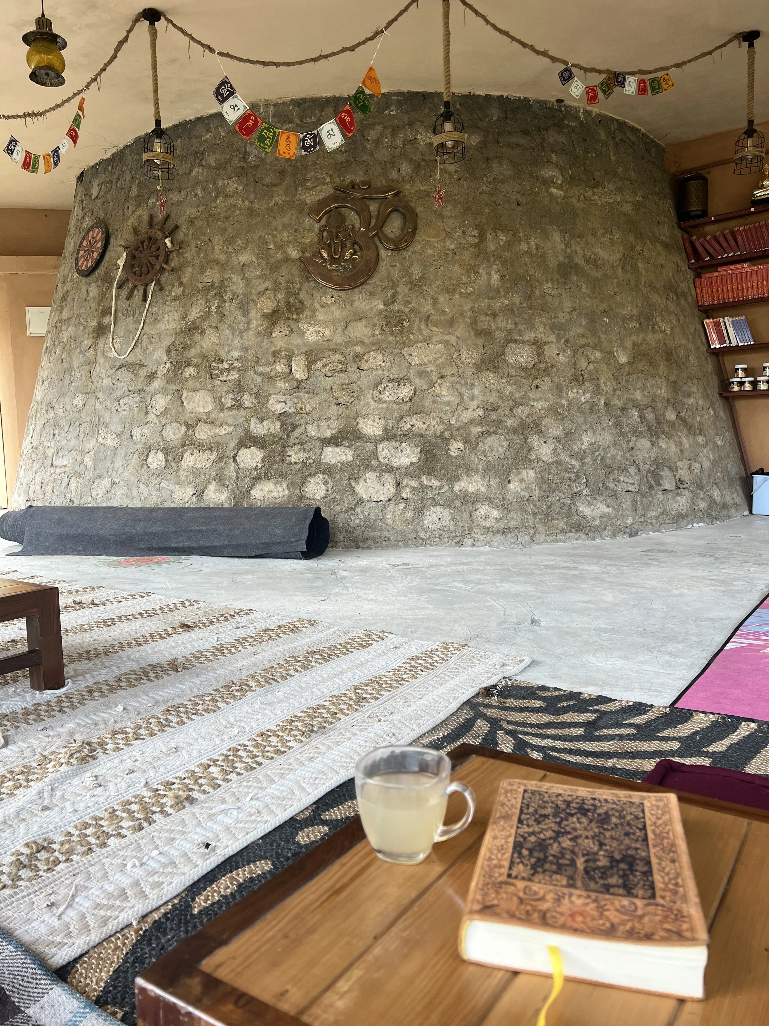 A tea and a book on the floor and a circular, stone wall further in the distance.