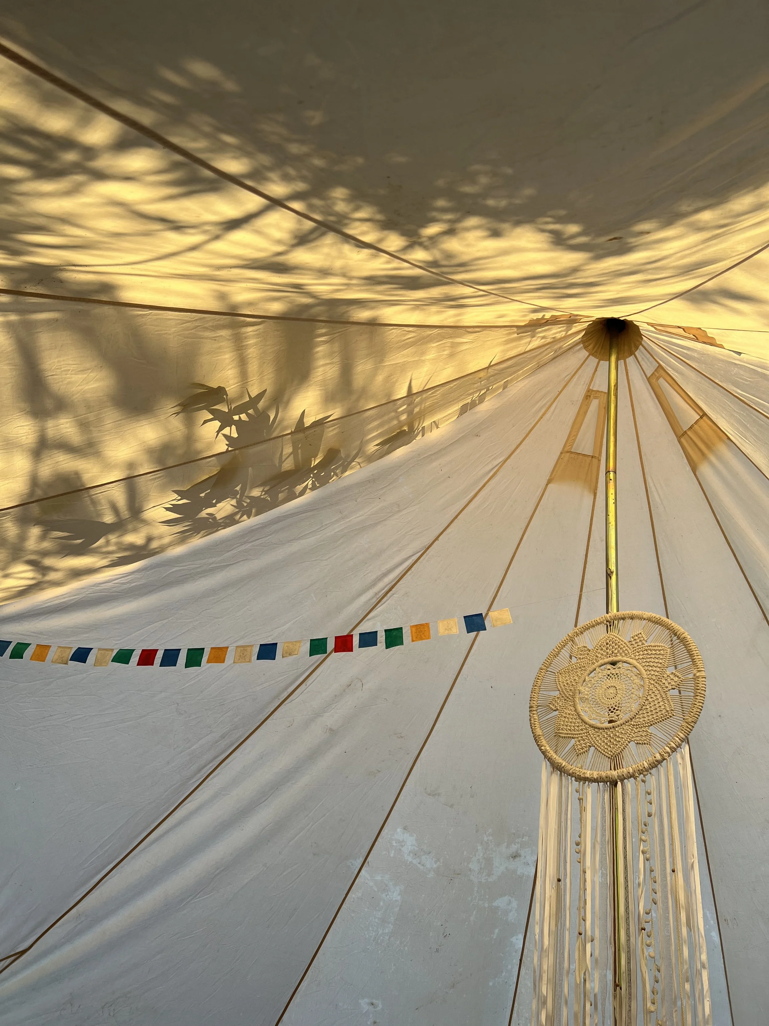 The sunlight and shadows coming through a tent with a colorful banner and macrame art.