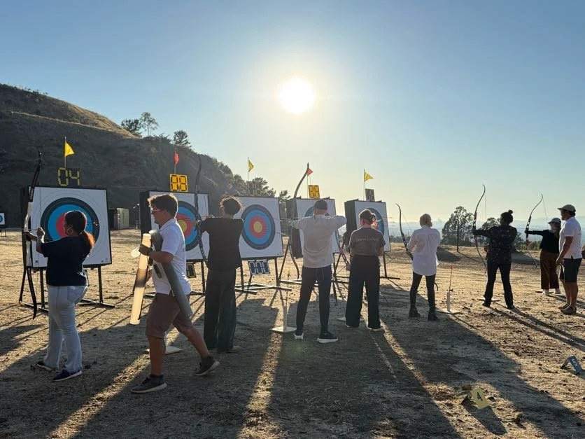 People participating in an outdoor archery target practice session during sunset with targets set up on a hillside.