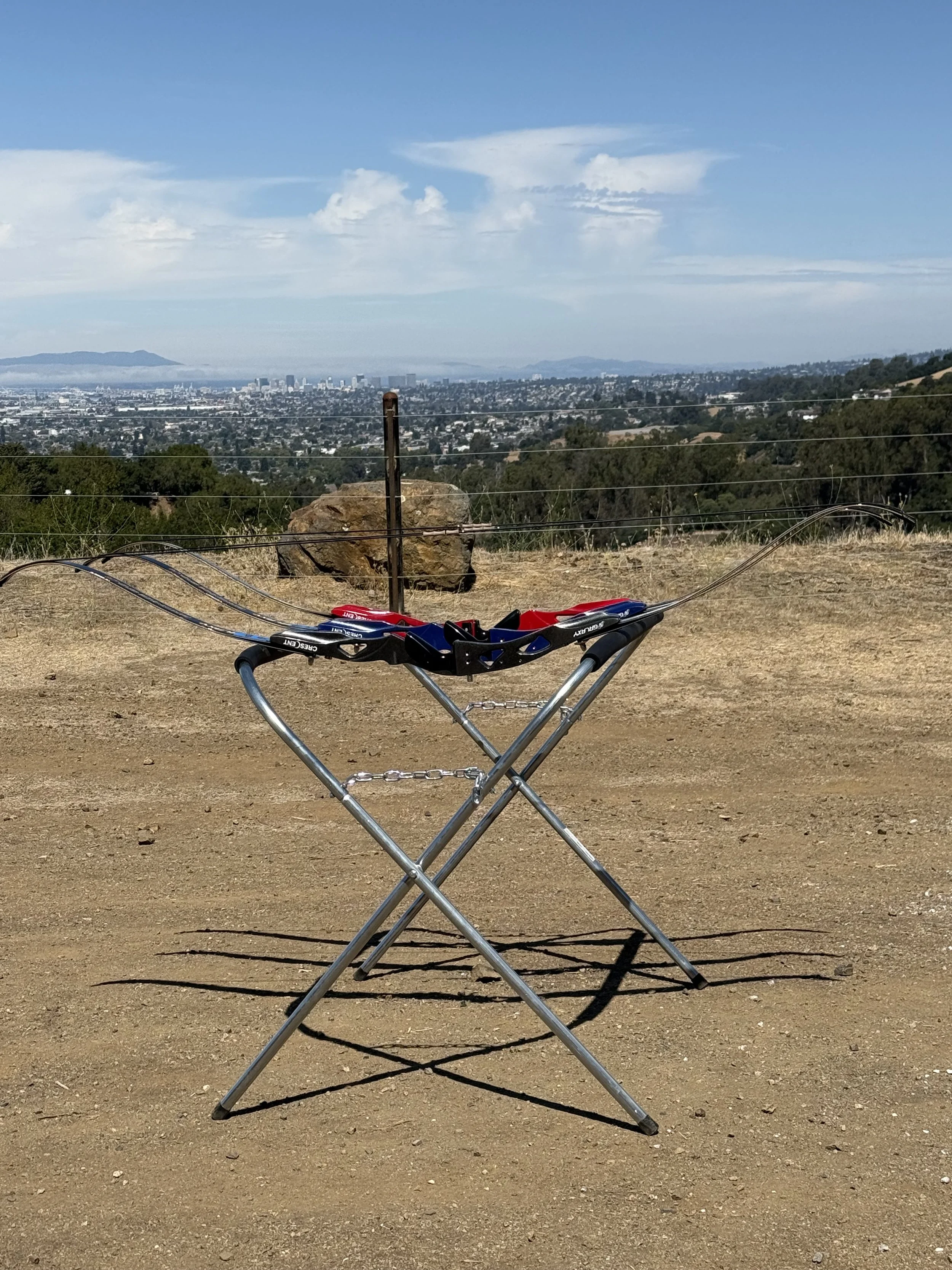 A mountain bike helmet placed on a collapsible table outdoors with a city skyline, hills, and partly cloudy sky in the background.