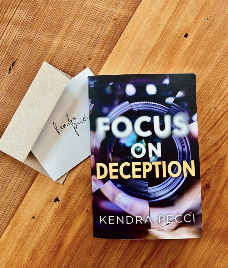 Person reading an e-book on a Kindle device while sitting on a beige couch. Focus on Deception is also available on Kindle Unlimited.