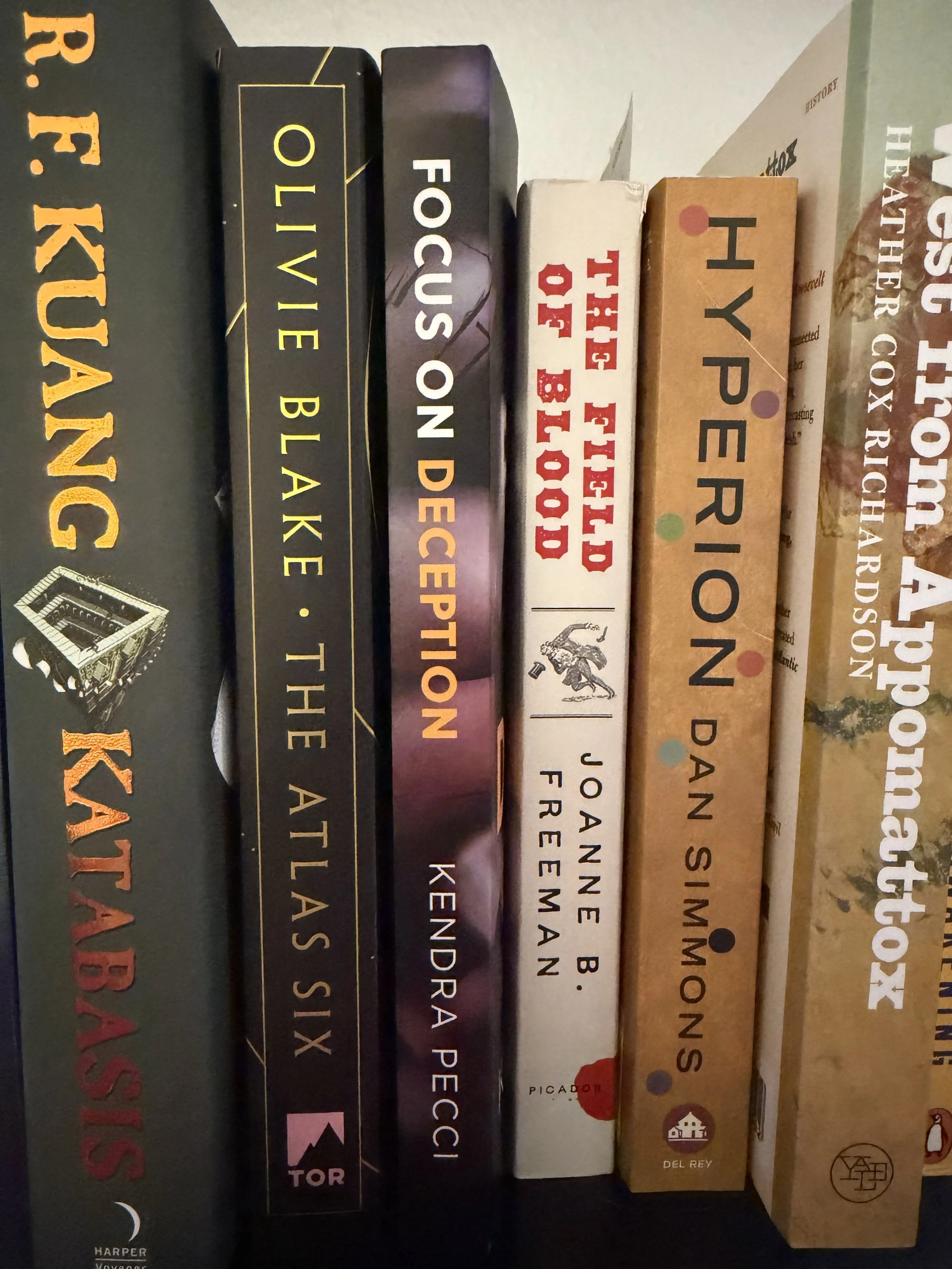 A close-up of a row of books on a shelf, with new release 'Focus on Deception' surrounded by literary classics and other favorites.