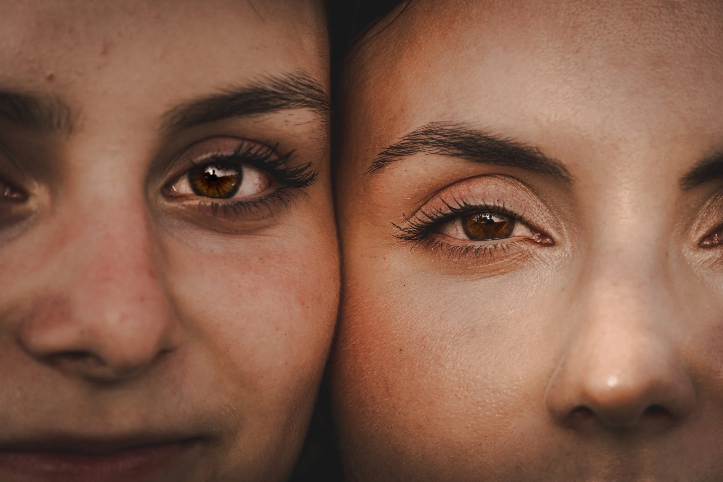 Close-up of two women's faces, focusing on their eyes and noses, with their faces touching.