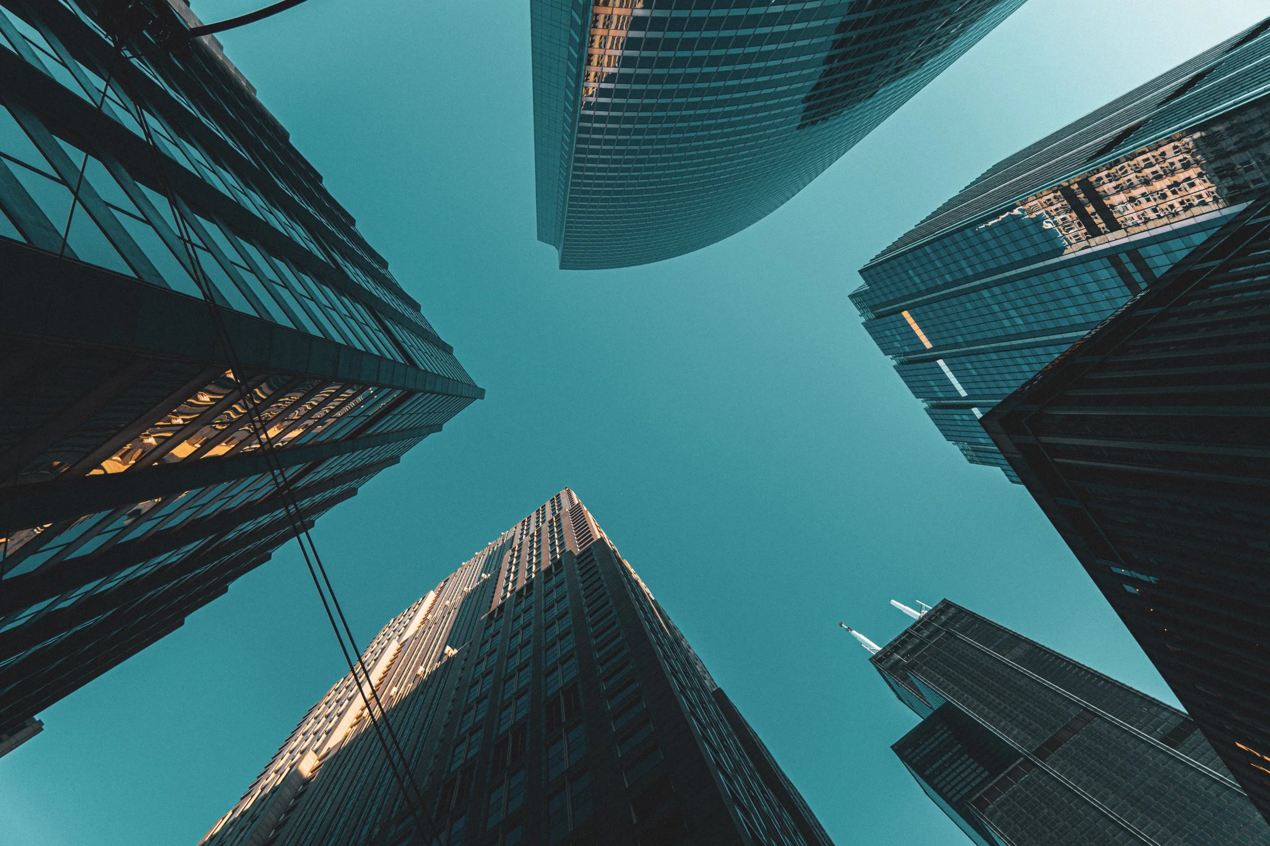 Looking up at tall modern skyscrapers under a clear blue sky in a city.