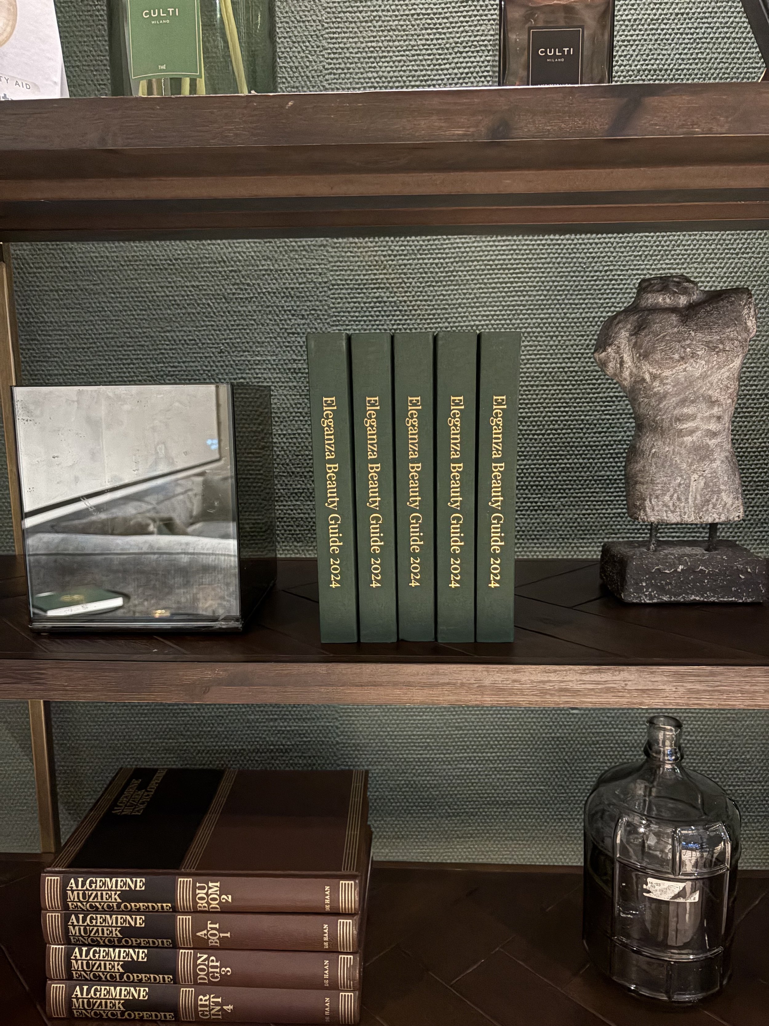 Bookshelf with Eleganza Beauty Guides, stone sculpture, mirrored cube, and glass bottle