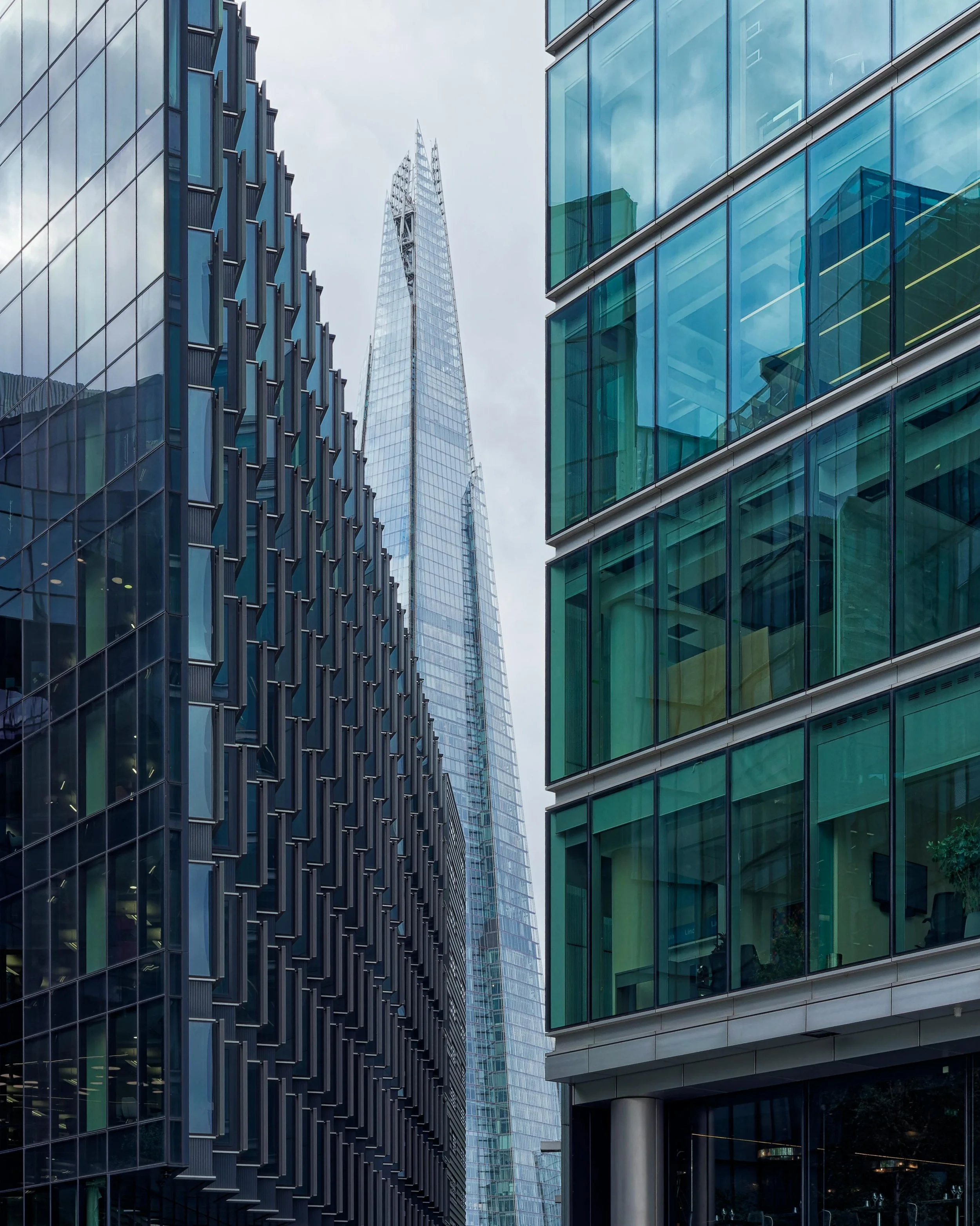 Blick von unten auf den Shard in London, eingerahmt von zwei Glasfassaden moderner Bürogebäude, als Symbol für unternehmerische Entscheidungskontexte.