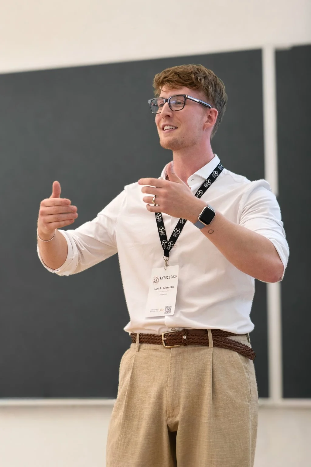 Luc Albrecht in weißem Hemd und brauner Hose vor einer schwarzen Tafel bei einem internationalen Vortrag in Portugal.