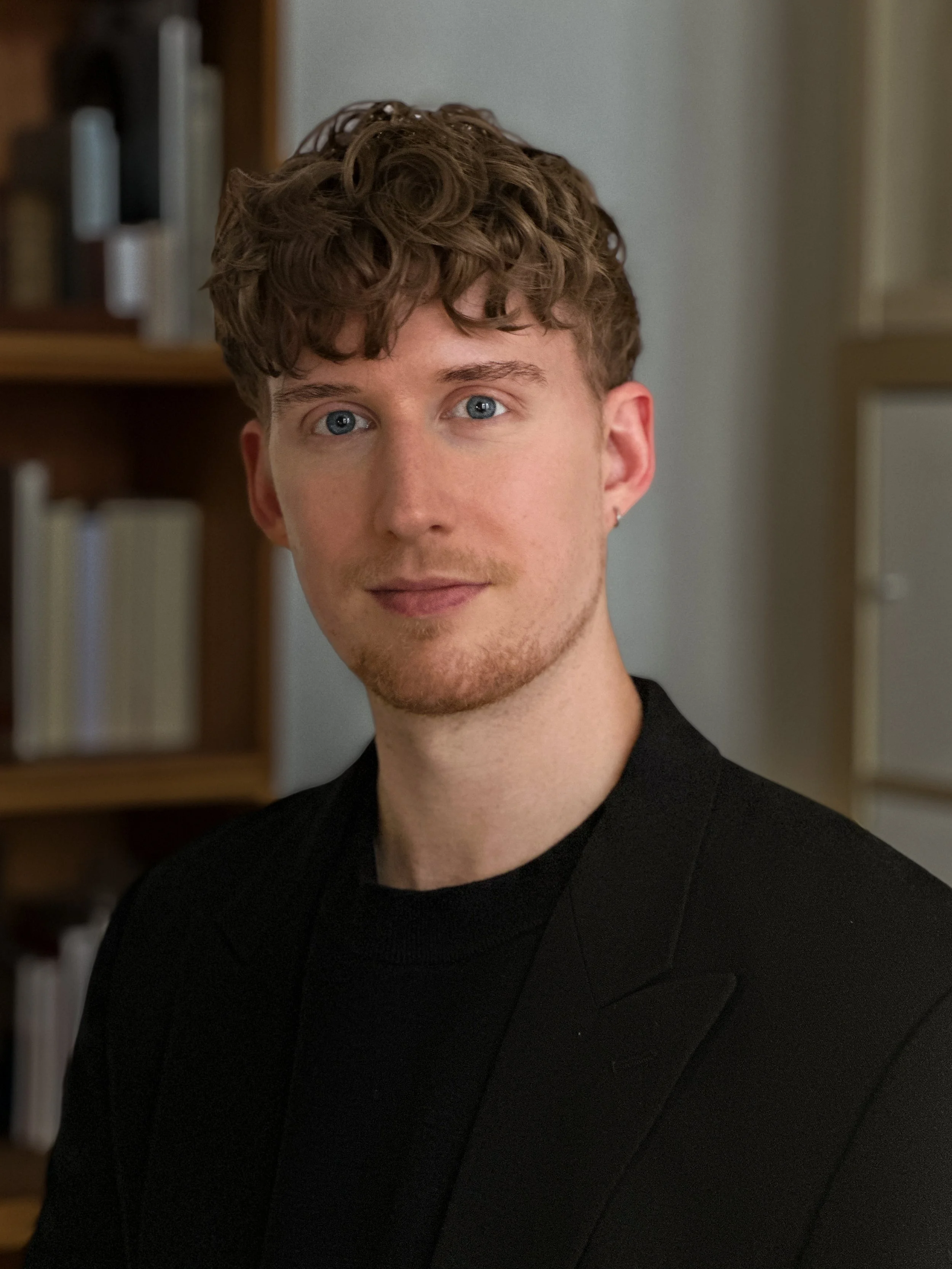 Porträt von Luc Albrecht im schwarzen Sakko vor einer Bücherwand.