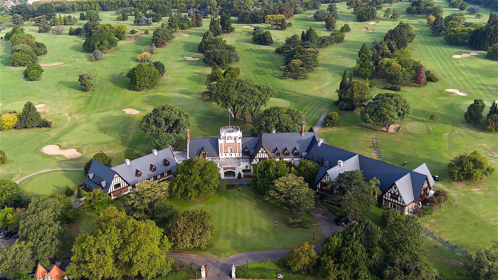 An aerial view of a large estate with a mansion surrounded by lush greenery and a golf course with multiple sand bunkers.