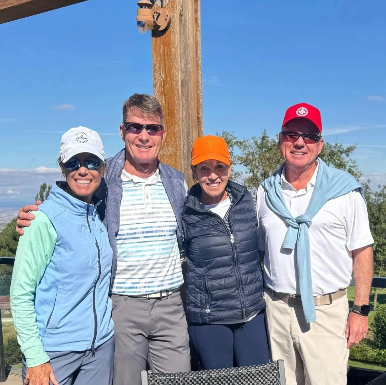 Four people standing on a golf course in Madrid holding golf clubs, with trees and a cloudy sky in the background.