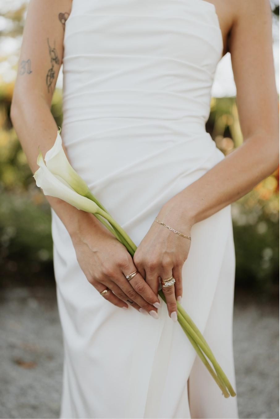 Bride with arm tattoos in white strapless gown holding long stem calla lilies.
