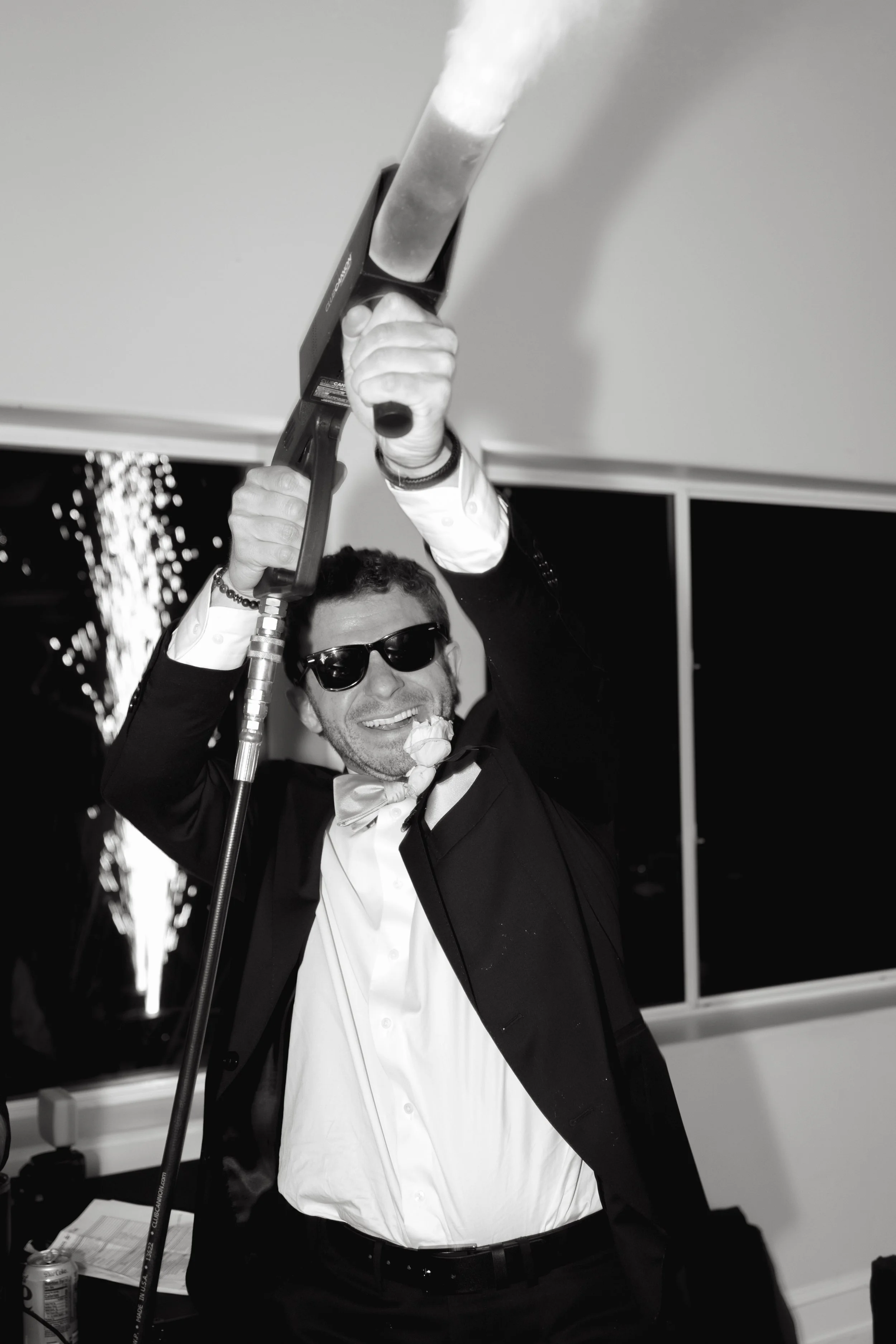 A man in a tuxedo holding a blowtorch and smiling at a celebration party.