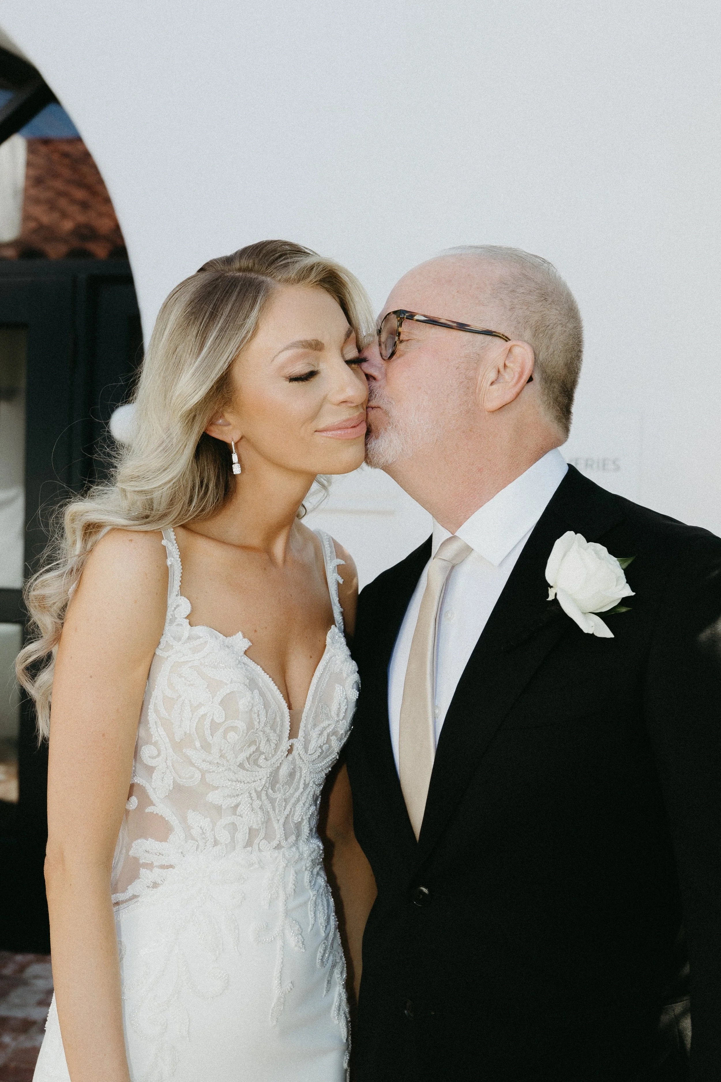 Bride and an older man, likely her father, sharing a tender moment at her wedding, with the man kissing her on the cheek.