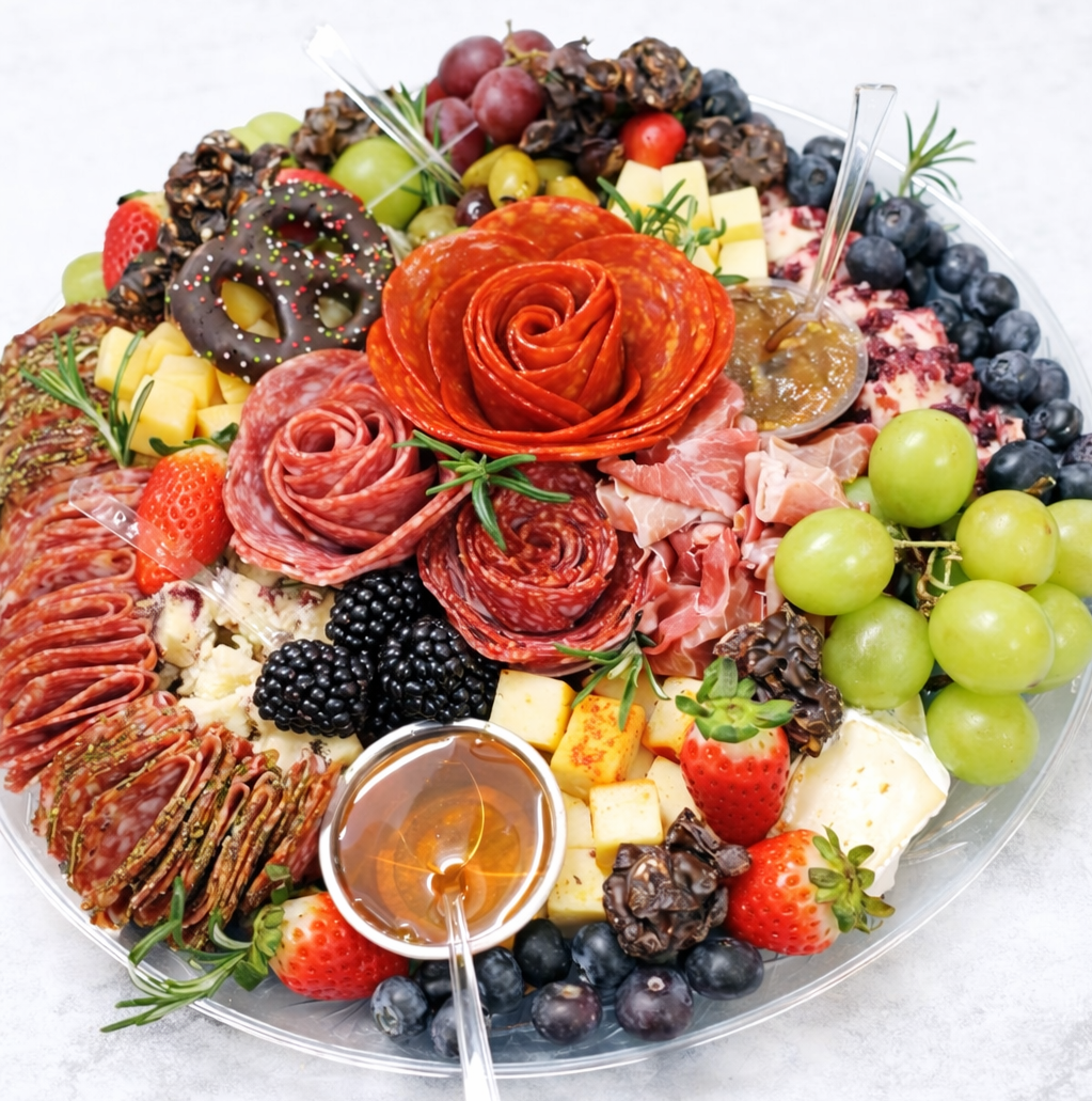 An elegant charcuterie board featuring an assortment of fresh fruits, cheeses, cured meats, chocolates, and honey, garnished with sprigs of rosemary.