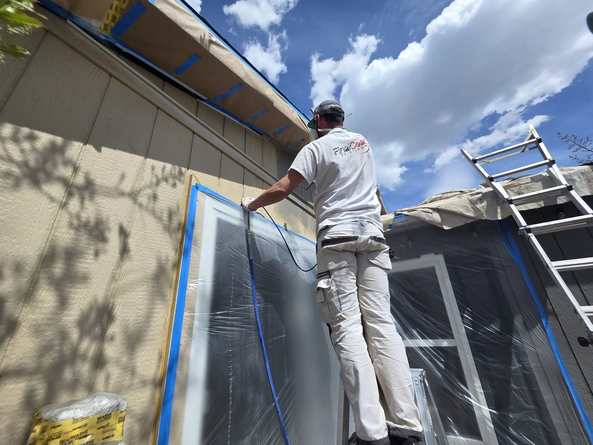 Painter in Canmore spraying exterior siding after carefull preparation