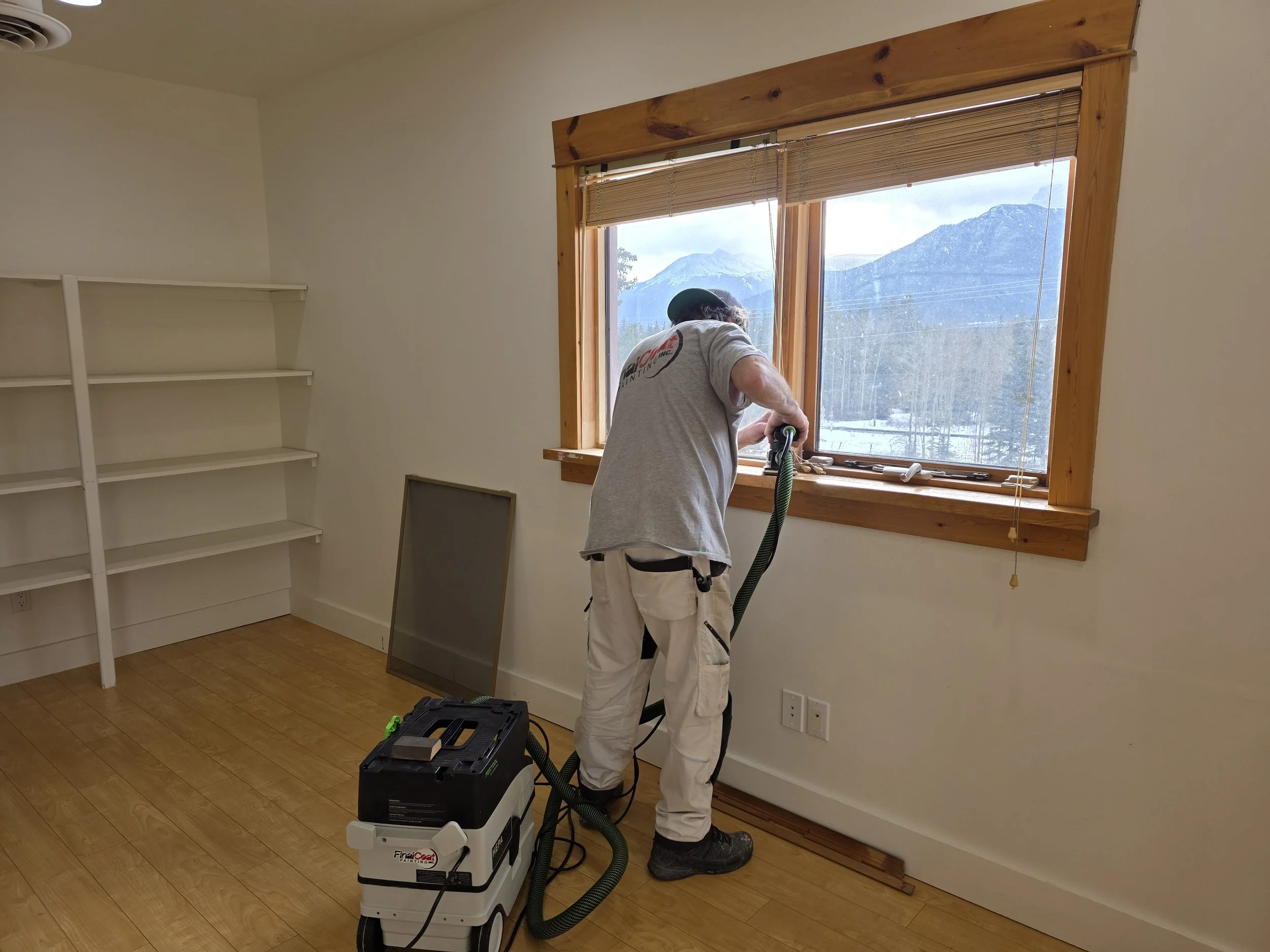Skilled painter in Canmore using high-performance equipment for sanding wooden window sills