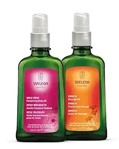 Two green bottles of Weleda massage oils with white spray caps, one labeled 'Wild Rose' and the other 'Arnica,' displayed against a plain white background.