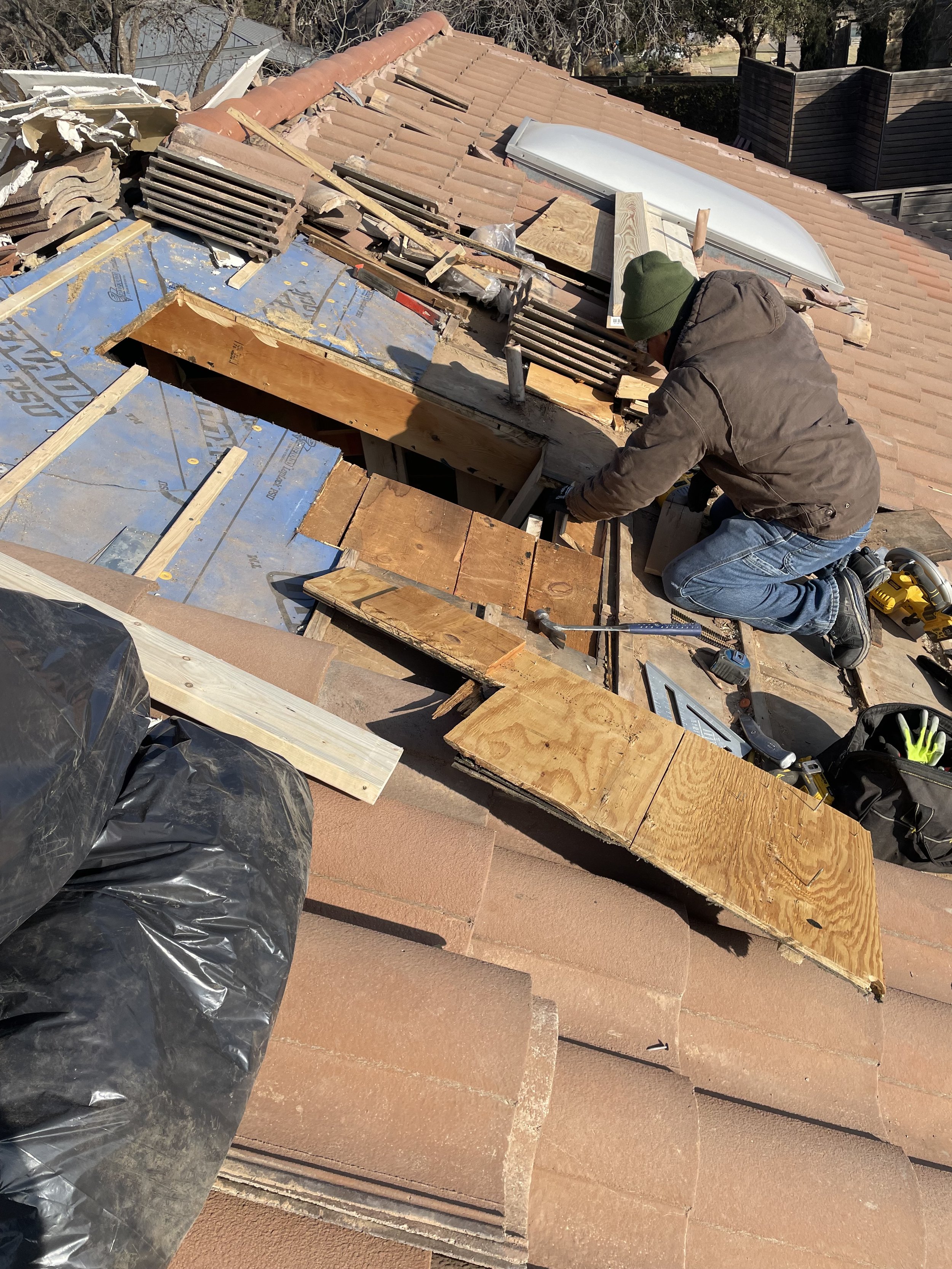 Roof repair with a worker fixing tiles and plywood on a residential rooftop.