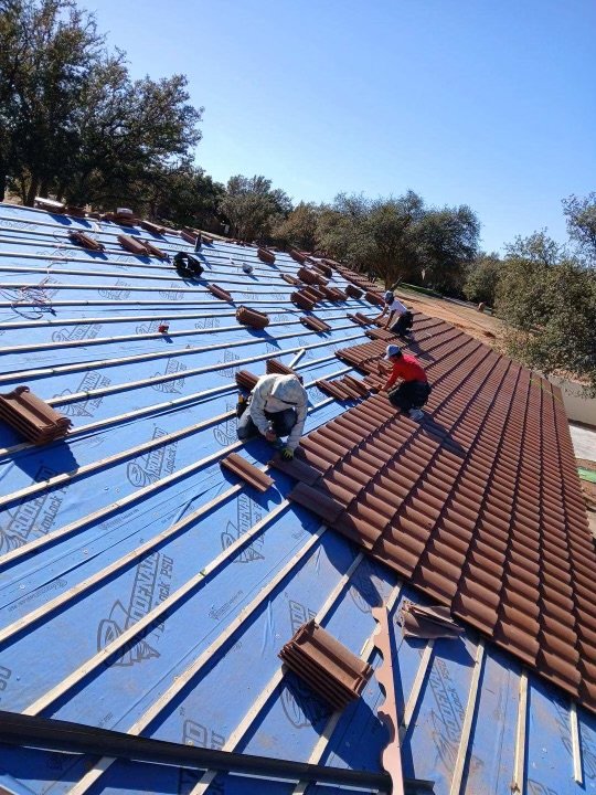 Roofers installing terracotta tiles on blue underlayment.