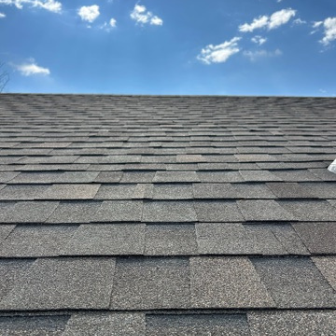 Gray asphalt shingle roof under a clear blue sky with a few clouds.