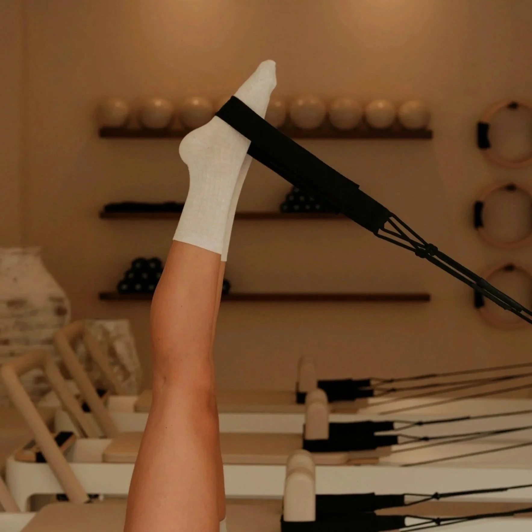 A woman exercising on a Pilates reformer machine in a fitness studio with beige decor and multiple Pilates reformers.