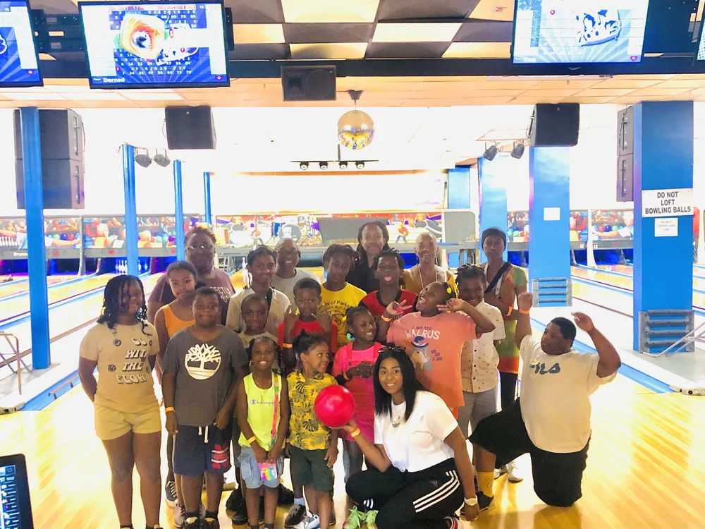 Youth and adults pose together at a bowling alley.