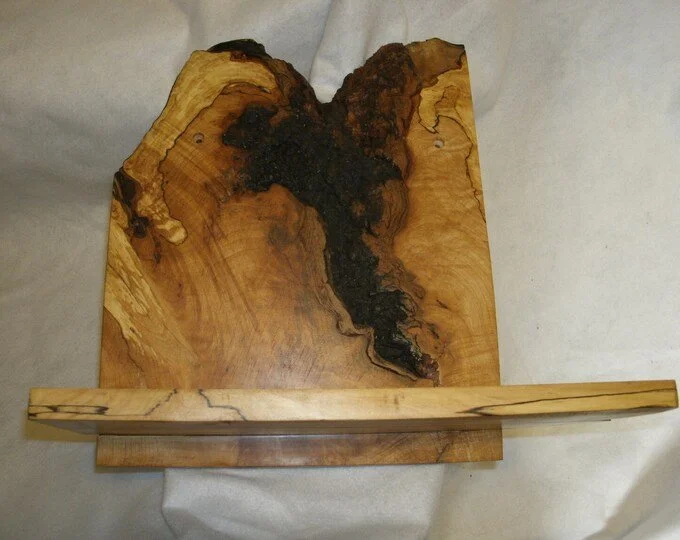 A wooden sculpture with natural wood grain and dark burned or stained areas, featuring an abstract, organic shape.