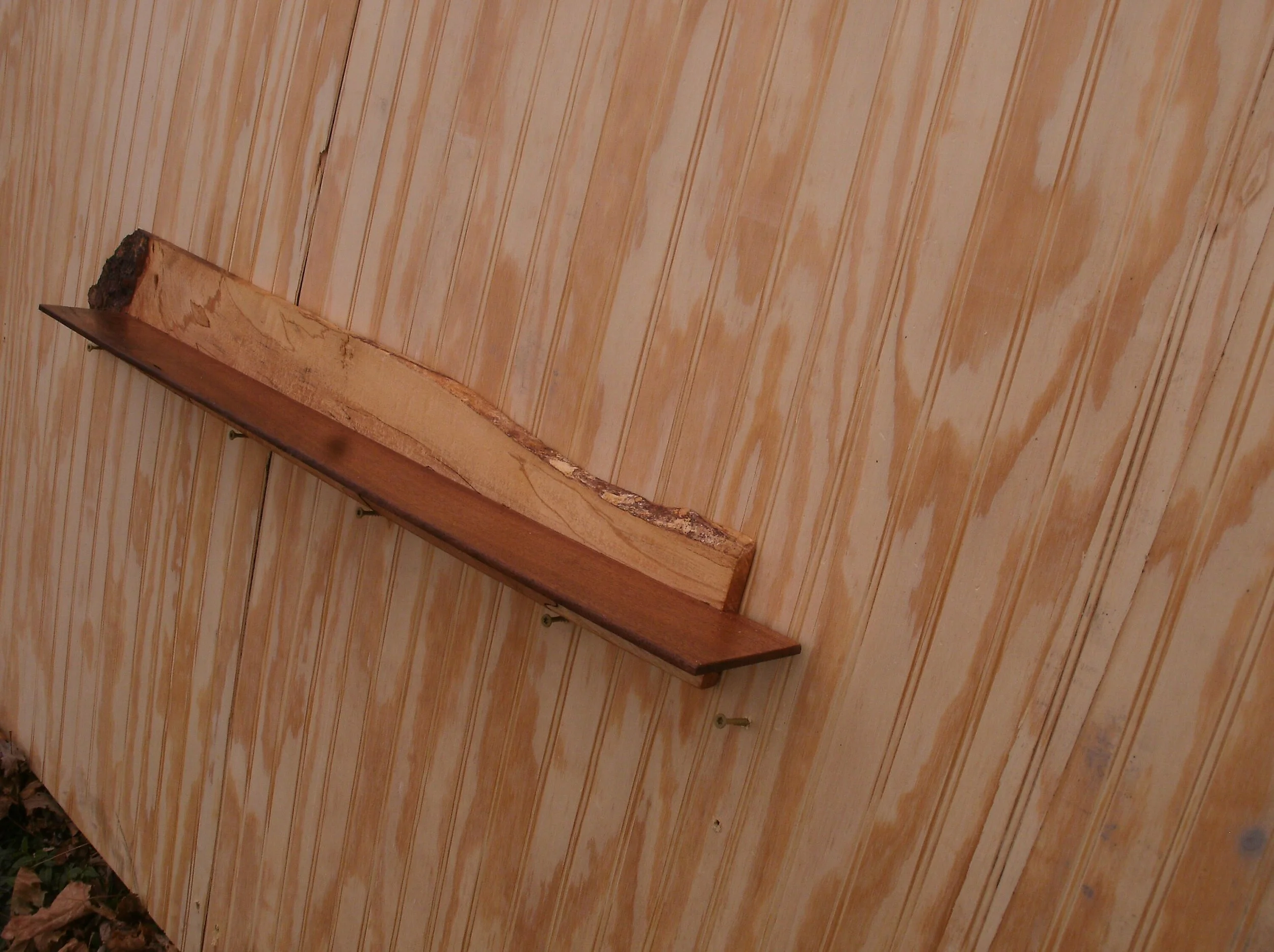A wooden shelf mounted on a wood-paneled wall with visible screws.