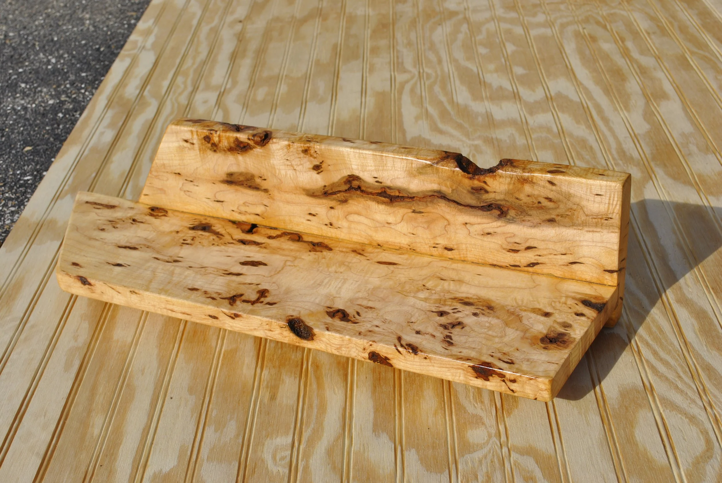 A rectangular wooden tray with a natural, uneven surface, placed on a wooden table outdoors.