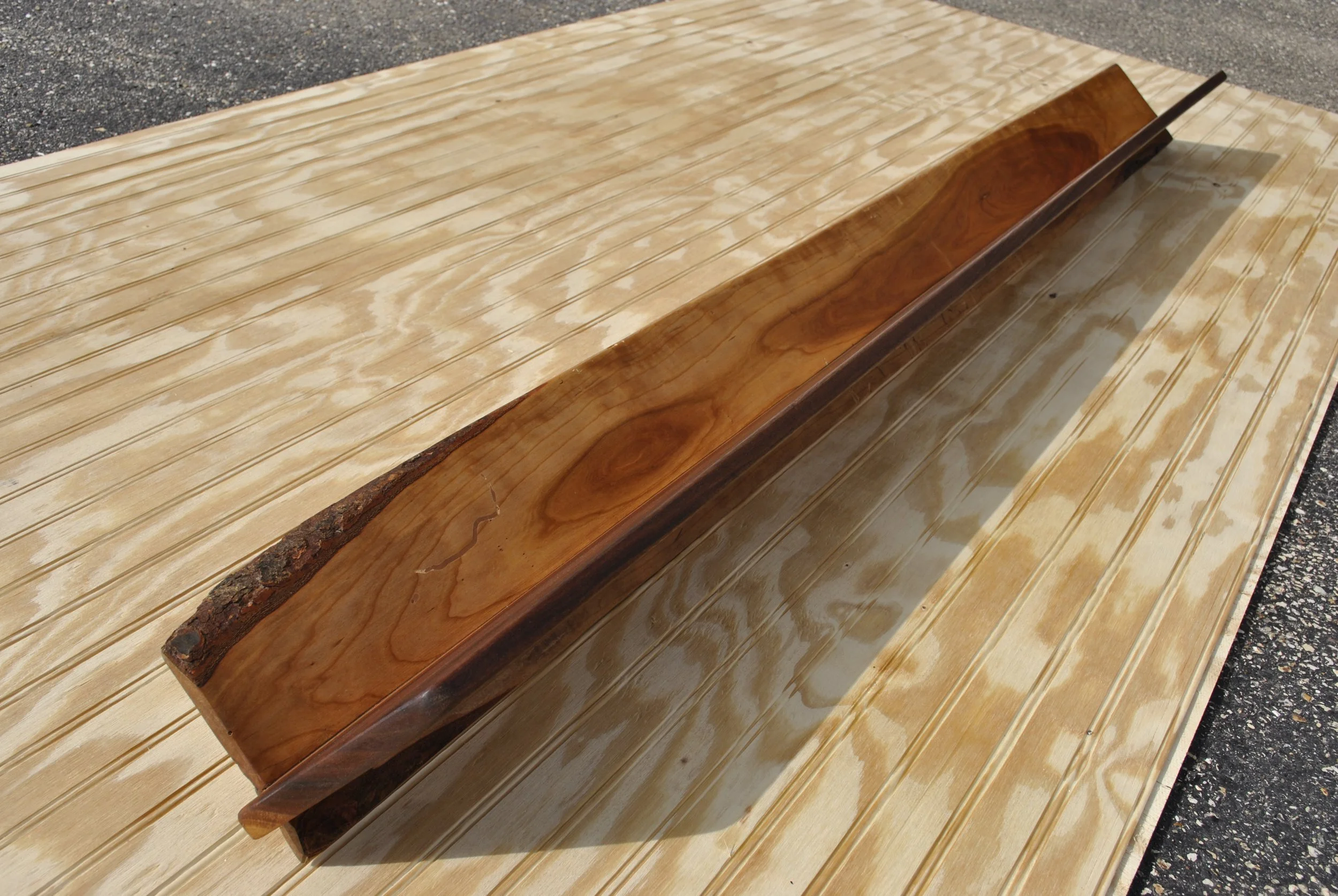 A polished wooden piece with a natural edge, placed on a light wooden surface outdoors.