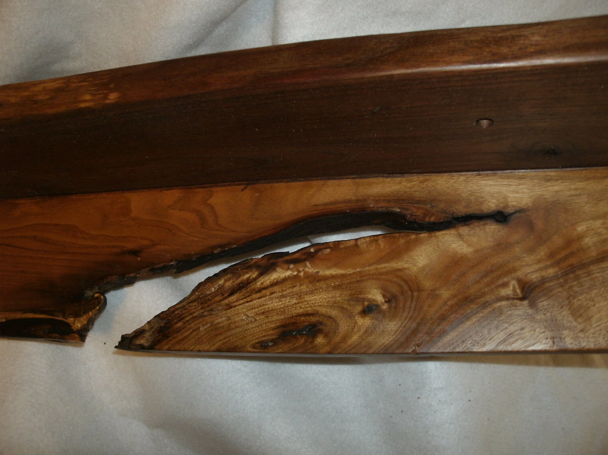 Close-up of a wooden board with a natural edge, showing wood grain and some dark resin or fill in the cracks.
