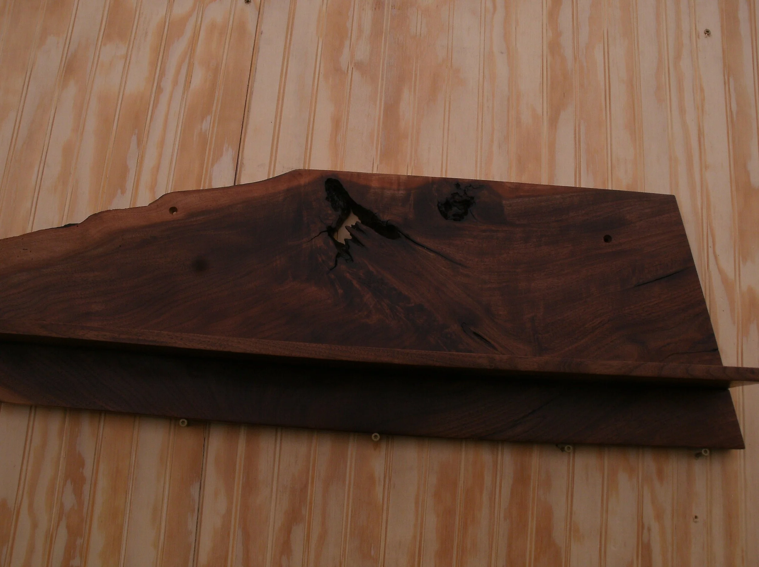 Close-up of a dark wooden shelf with a natural edge, mounted on a light wood-paneled wall.
