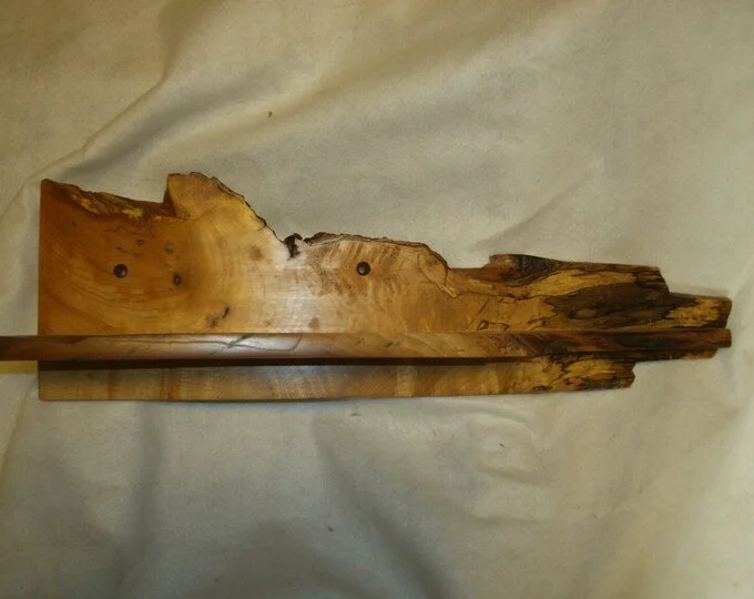 Wooden sculpture or carving with natural and rough edges, placed on a beige fabric background.