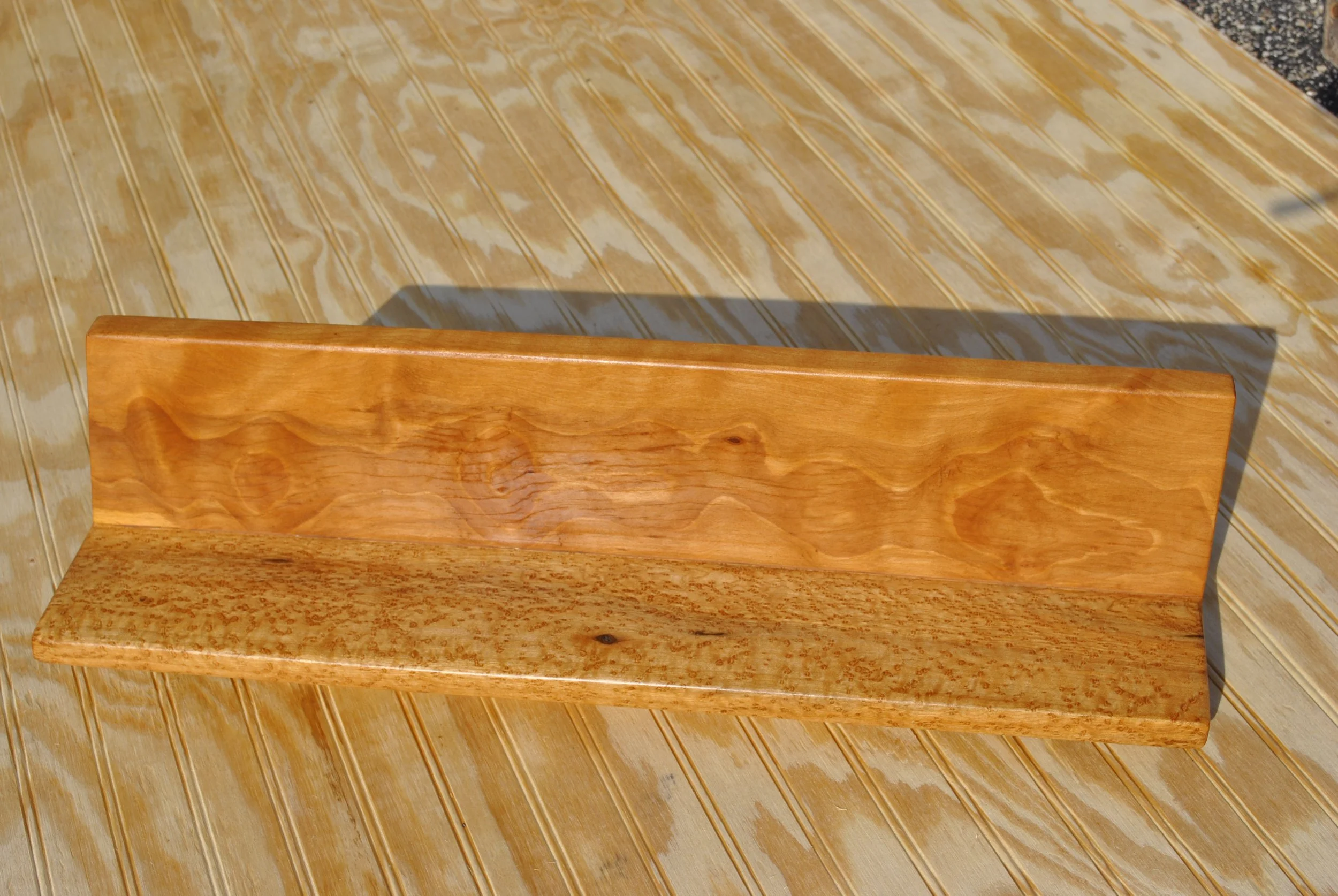 A wooden bench with a backrest, placed on a wooden surface.