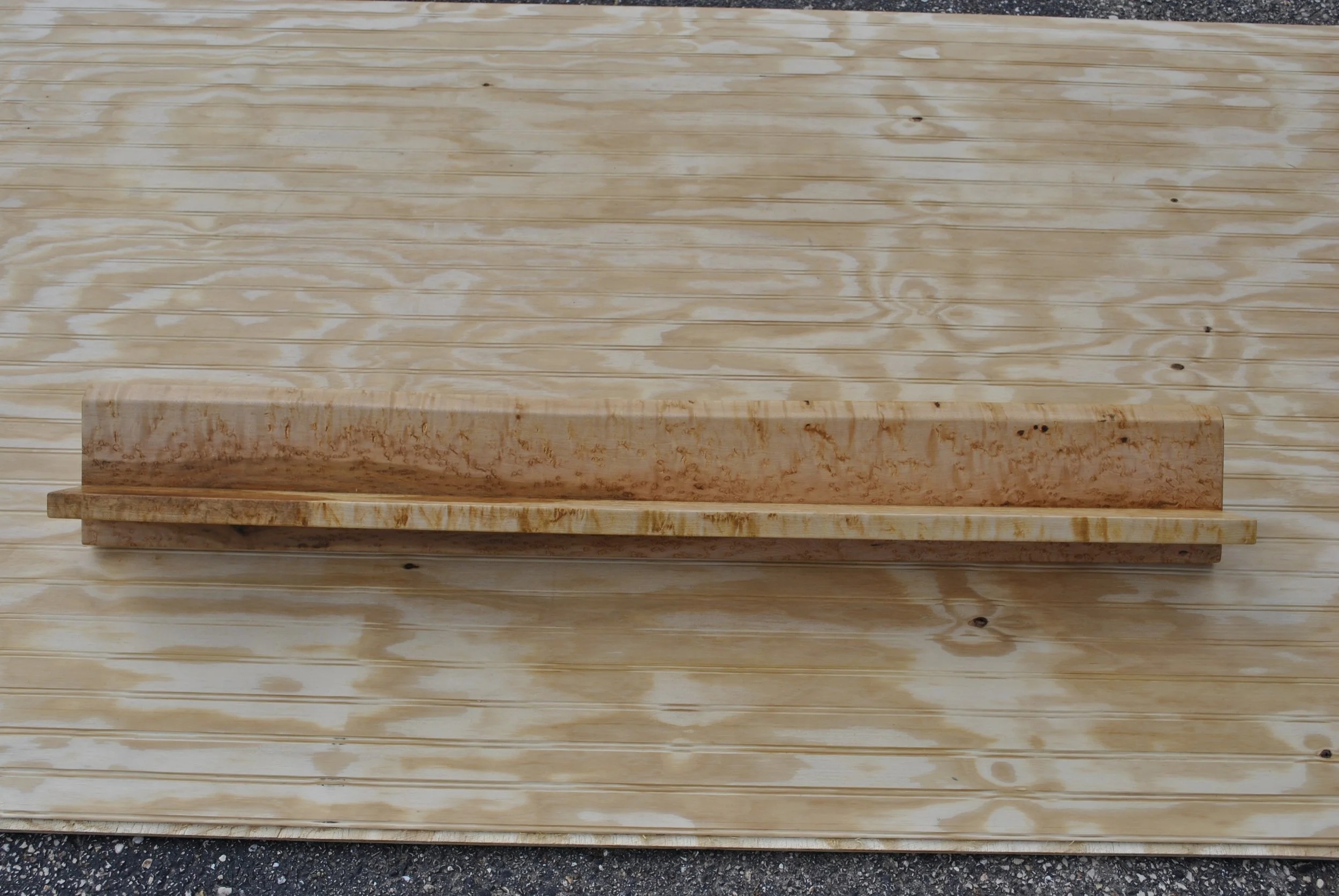 A piece of light-colored wood in front of a larger wooden surface.