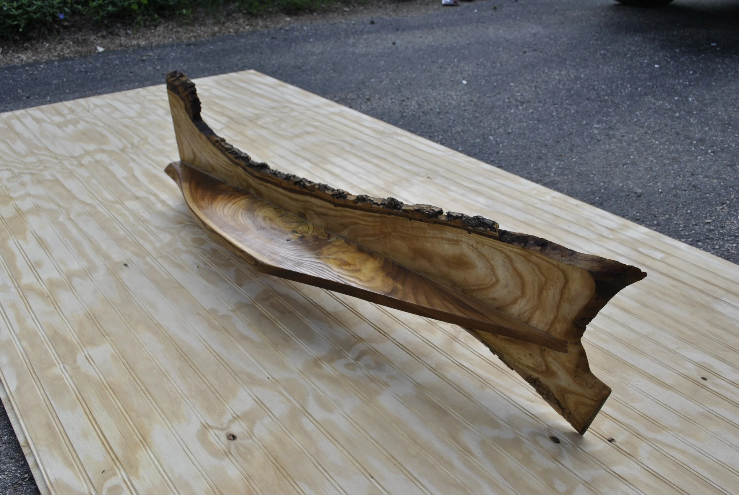 A handcrafted wooden bowl with bark edges, placed on a wooden board outdoors.