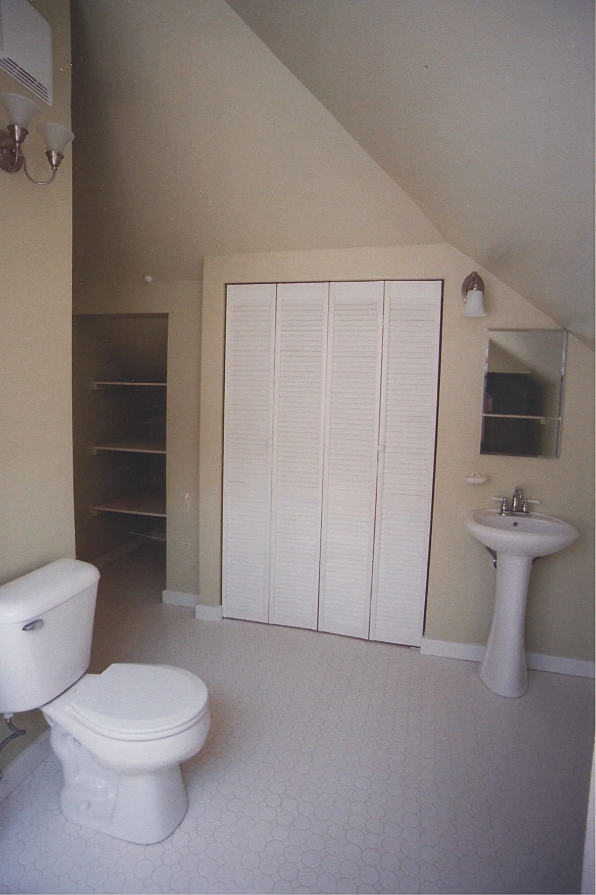 Toilet, sink, closet, and more built-in storage shelves to the left.