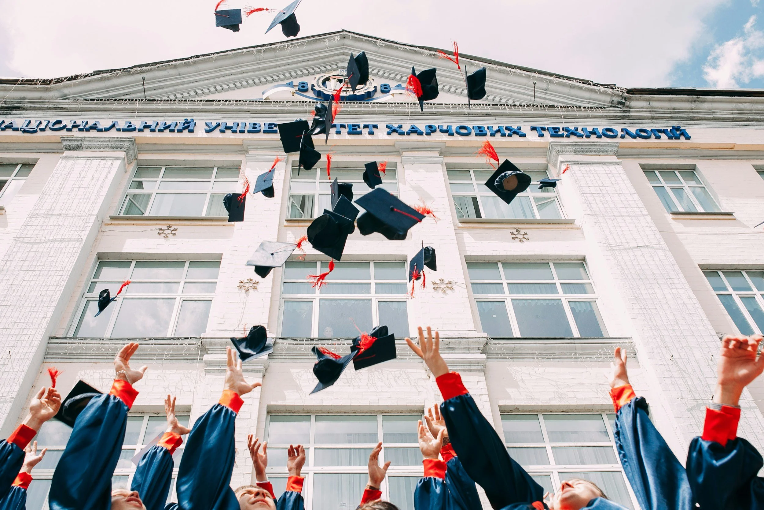 Graduates tossing caps in the air in front of a university building with Cyrillic lettering.