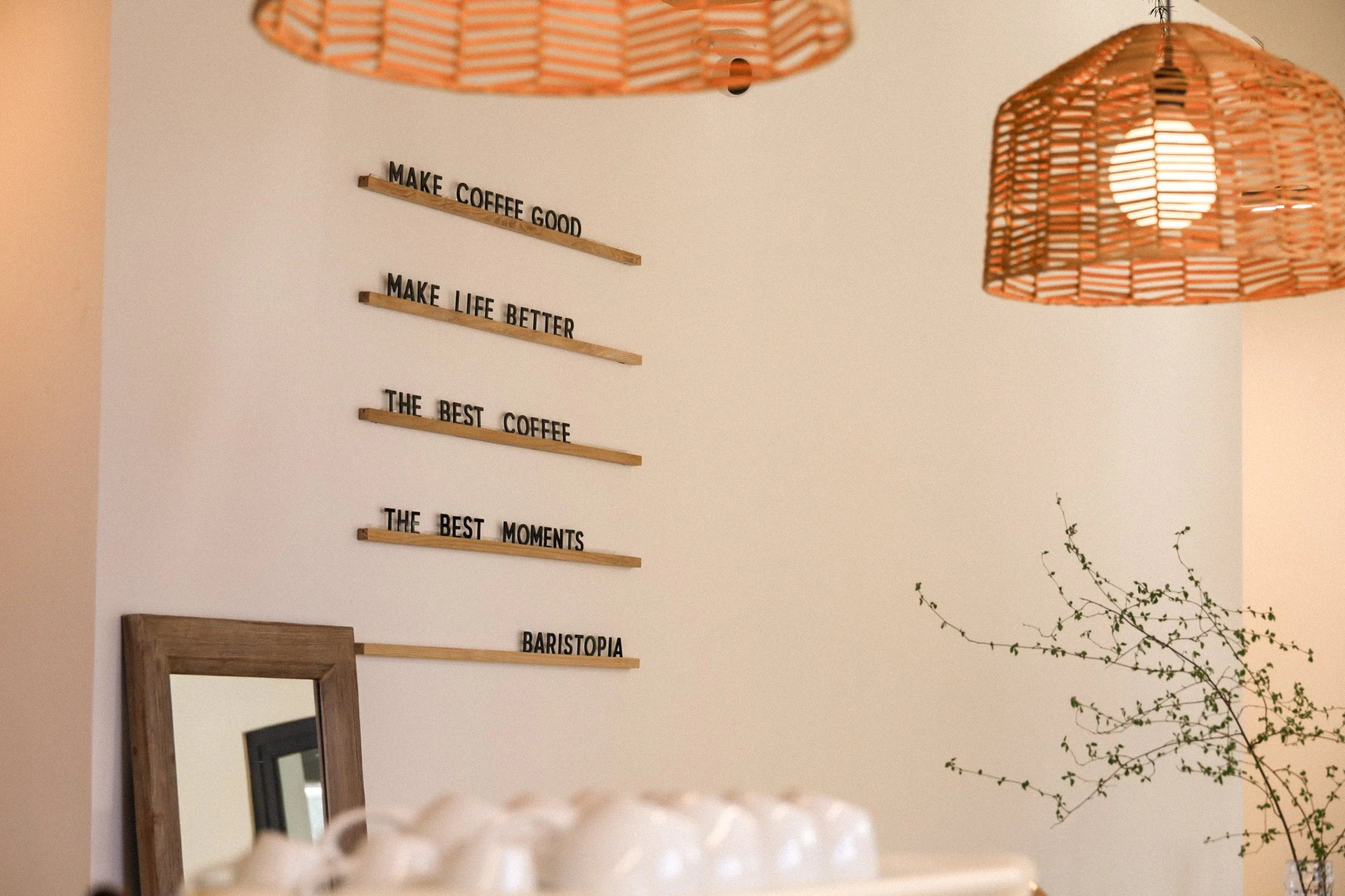 Cafe interior with motivational quotes on the wall, woven pendant lights, mirror, plant, and stacked cups.