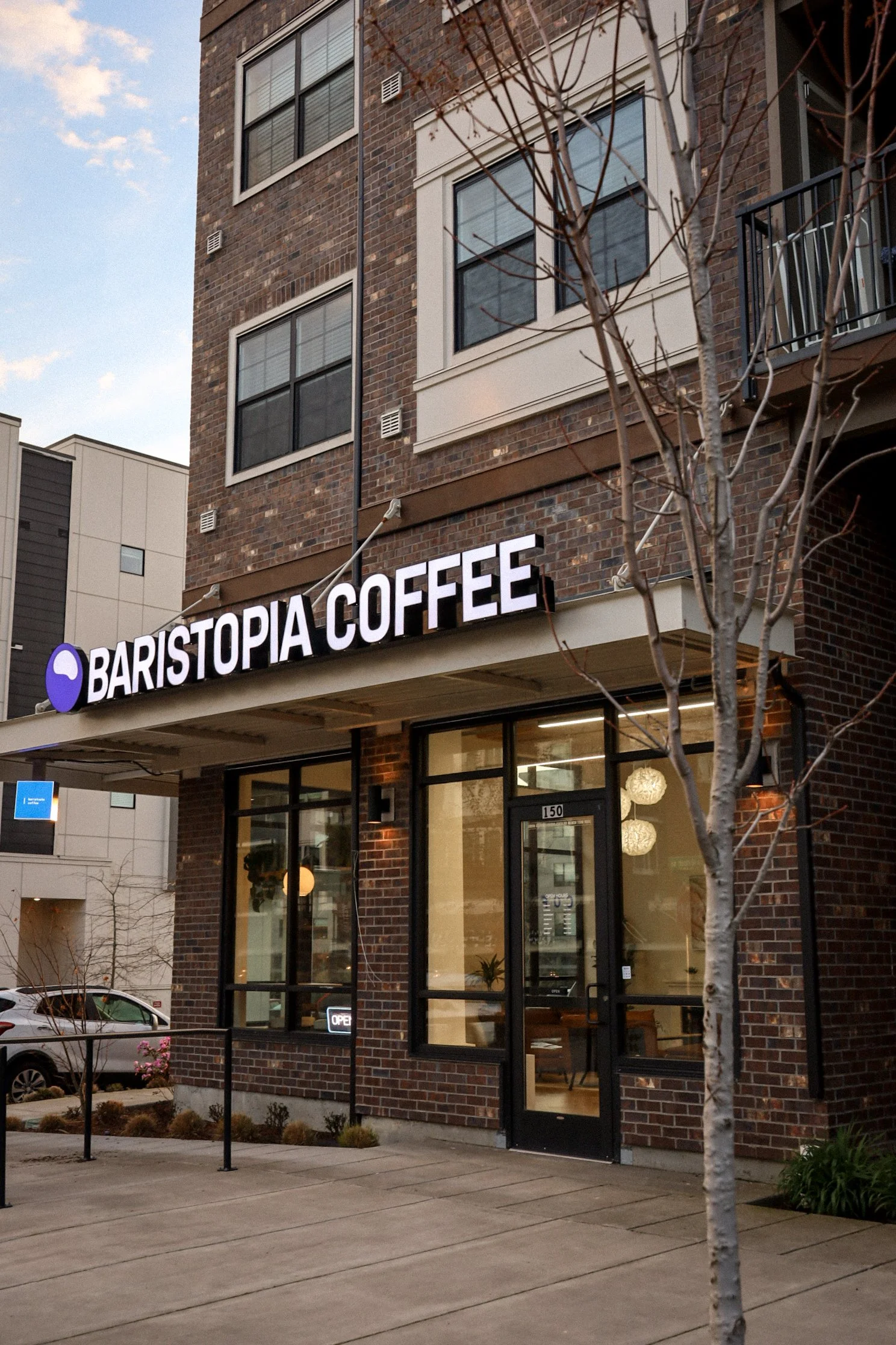 Exterior of Baristopia Coffee shop with brick facade, large windows, and "OPEN" sign.