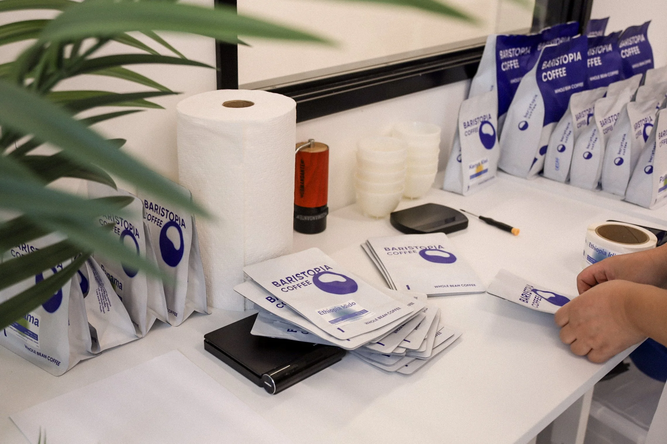 Person packing Baristopia Coffee bags on a table with coffee packaging materials and supplies.