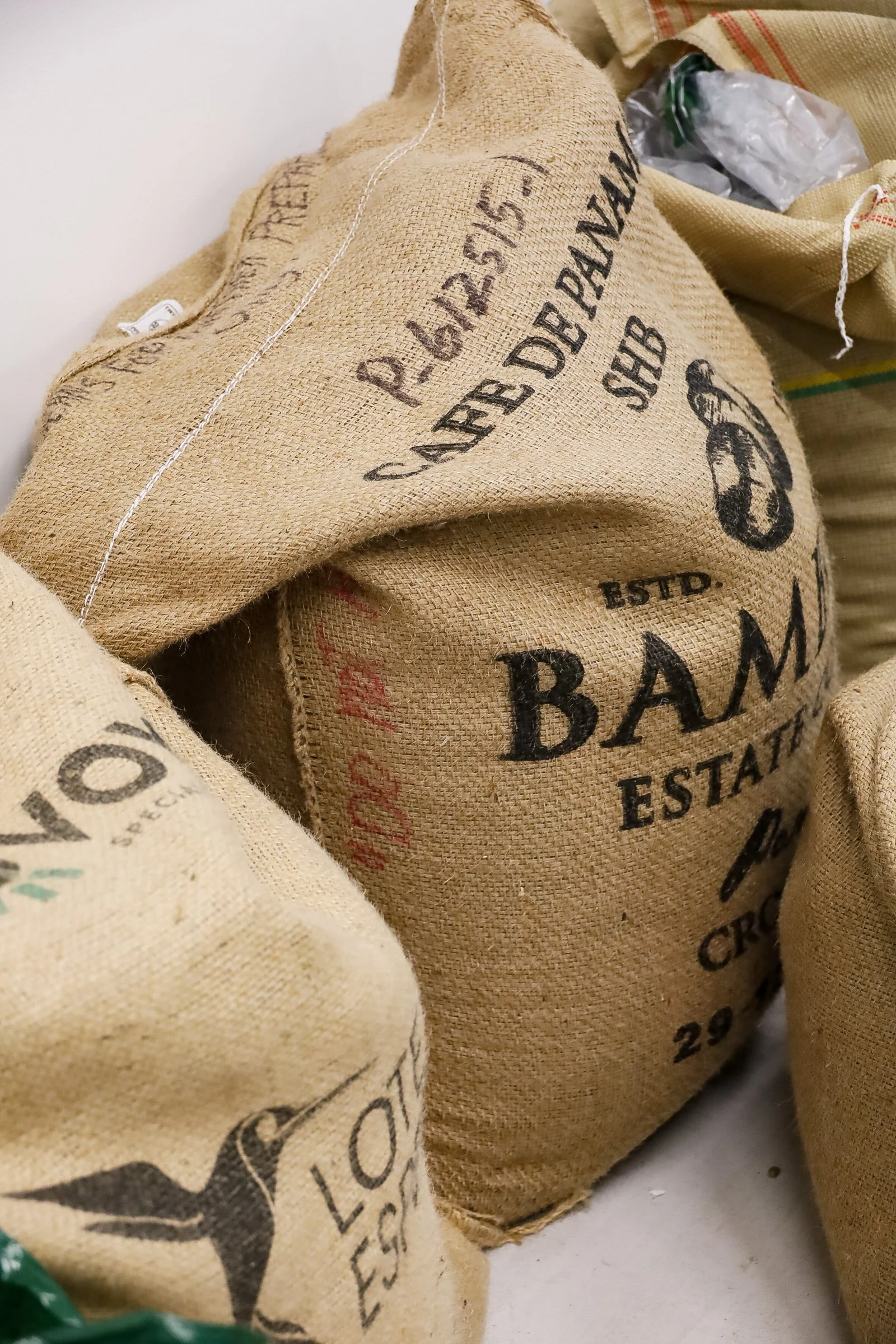 Burlap sacks labeled with coffee branding, including "Cafe de Panama" and "Bambu Estate Coffee."