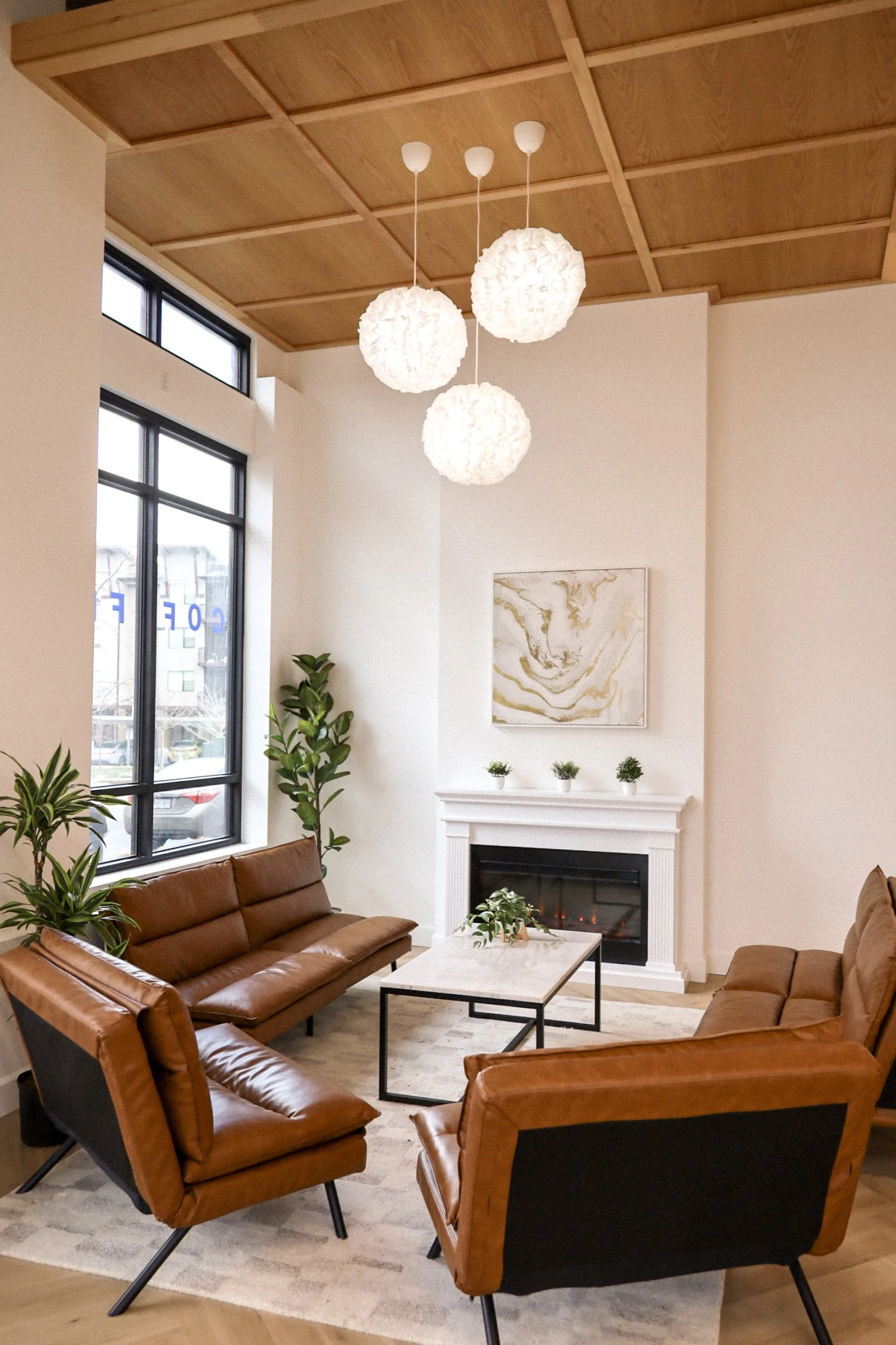 Modern living room like cafe with brown leather sofas, a white fireplace, abstract wall art, and large windows.