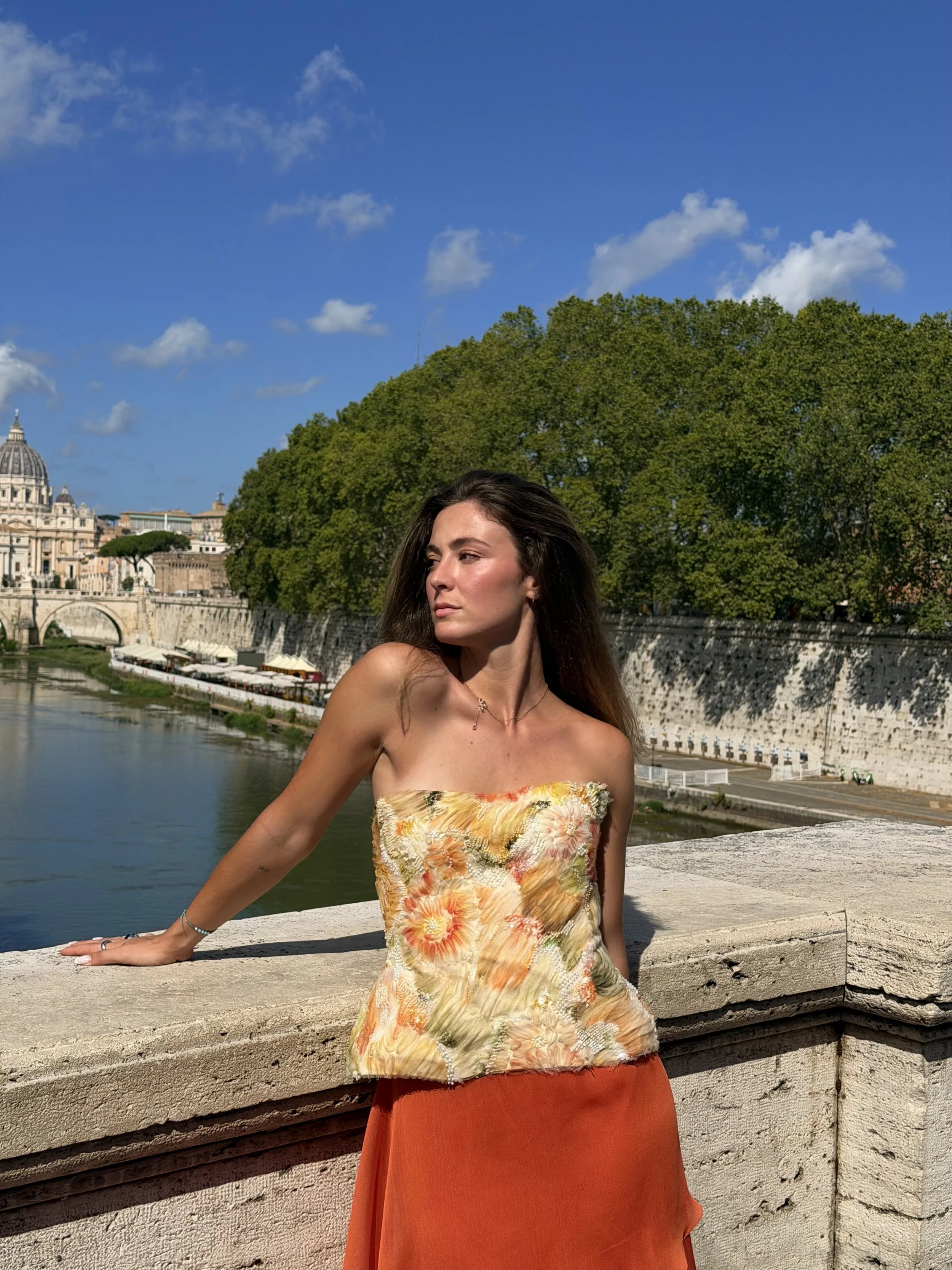 Mujer con vestido de flores anaranjado y fondo de árboles y río en Roma, Italia.