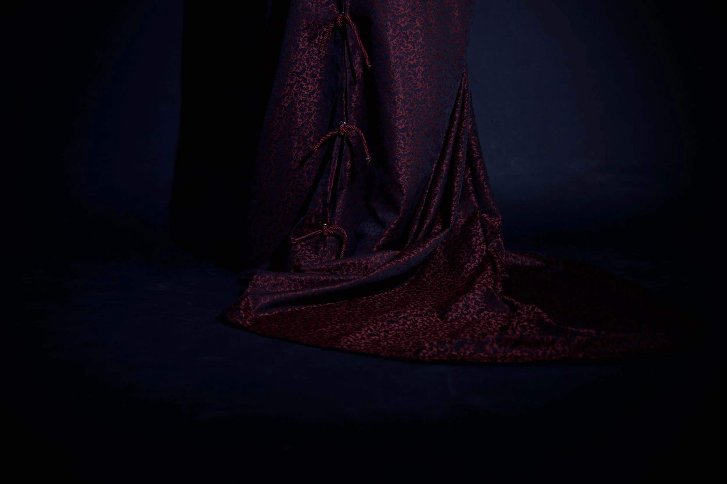 Tela de seda morada con patrones delicados, parcialmente extendida sobre el suelo, con pliegues y lazos decorativos. Fondo oscuro
