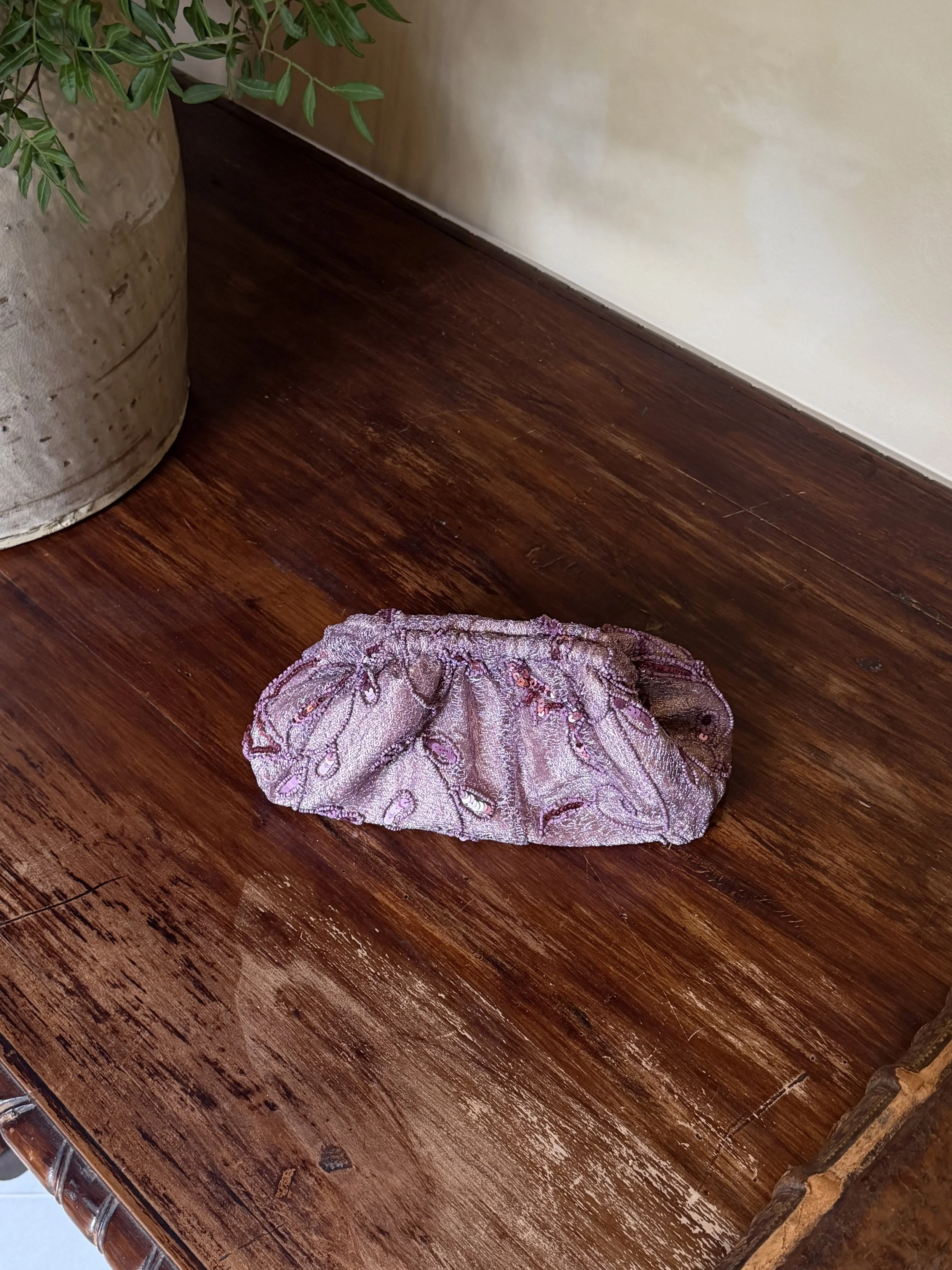 Un pedazo de tela rosa y morada con bordados y brillo, colocado en una mesa de madera oscura.