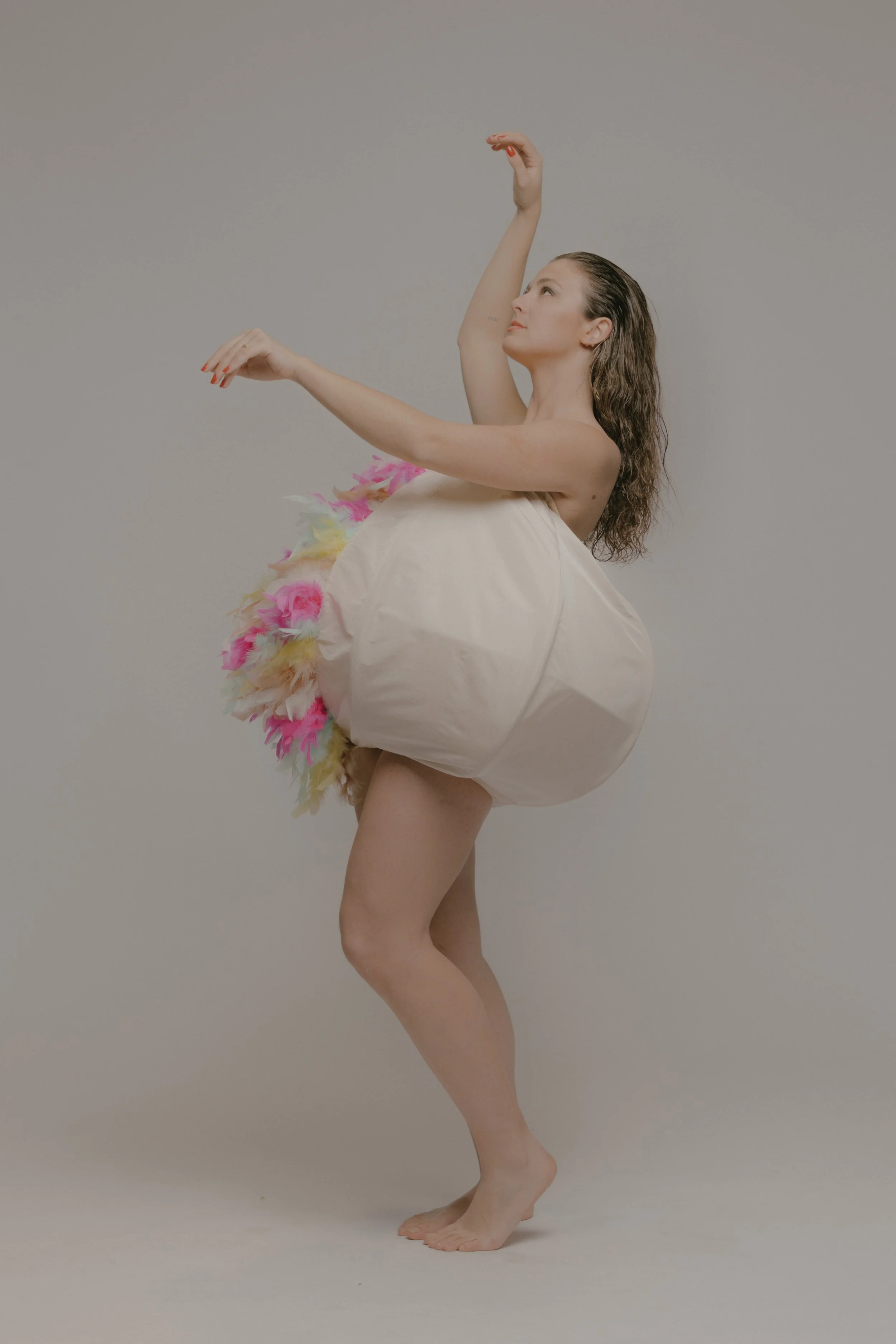 Mujer en vestido de bailarina posando con brazos elevados y una expresión serena, en un fondo gris.