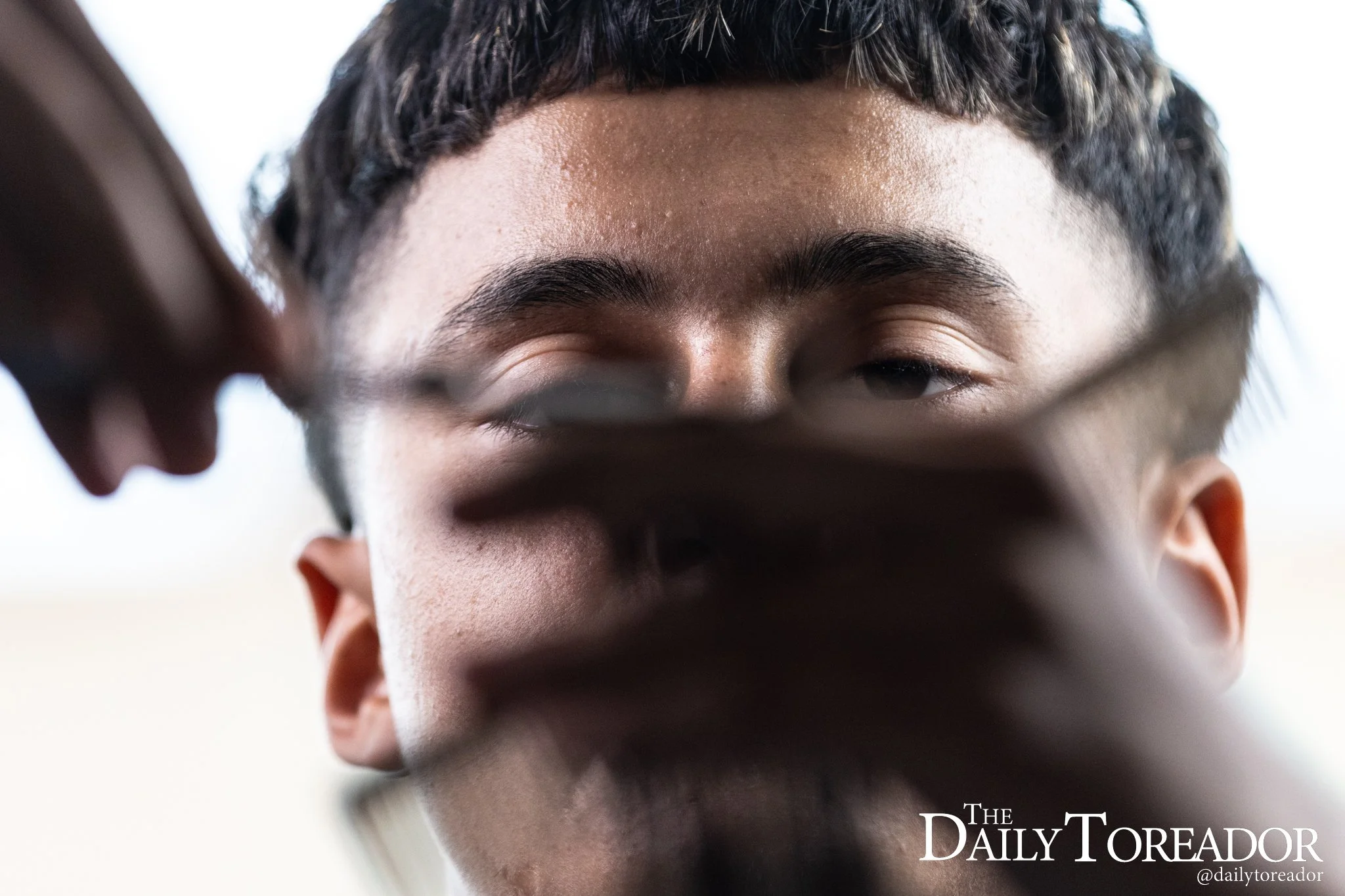 Texas Tech freshman business management major Juan Aguirre eyes the level of hair as he prepares to cut a handful of hair inside Coleman Hall, in Lubbock. Aguirre said as a barber he emphasizes the importance of the fine details, making sure that eve