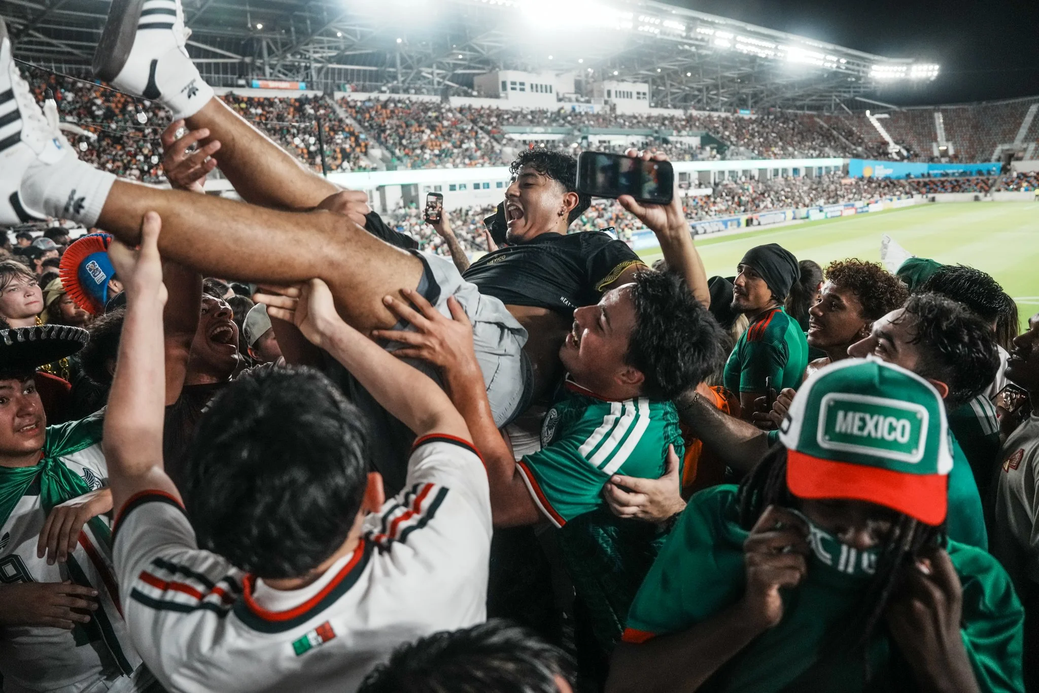 A group of soccer players celebrating on the field after a match, with many spectators in the stadium background.