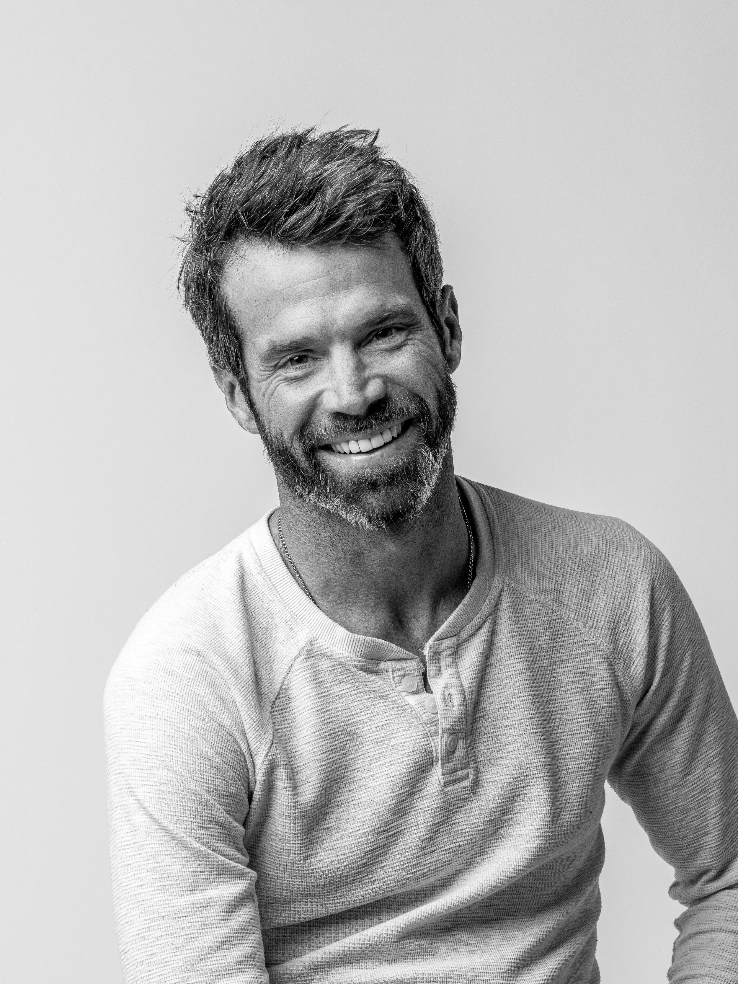 Black and white portrait of a smiling man wearing a henley shirt.
